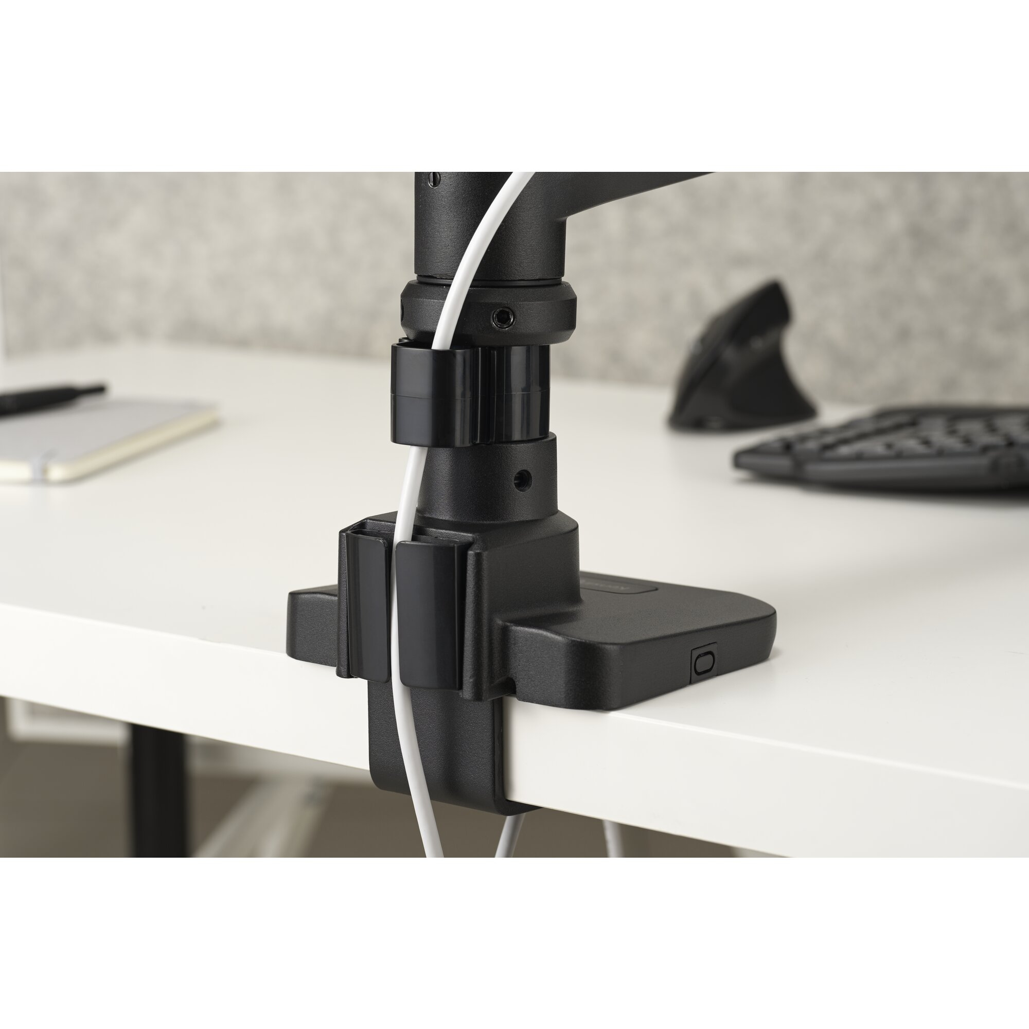 Un serre-câble de bras de moniteur noir fixe un câble blanc à un bureau blanc. Clavier et souris visibles.