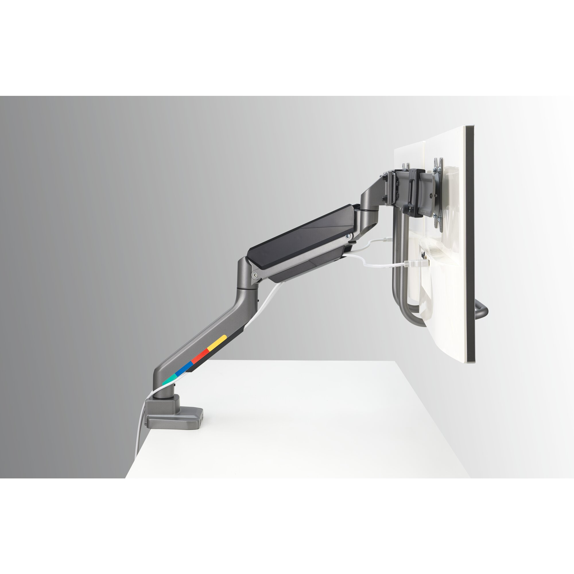 A monitor arm holds a white monitor above a desk. Gray arm with colored stripes.