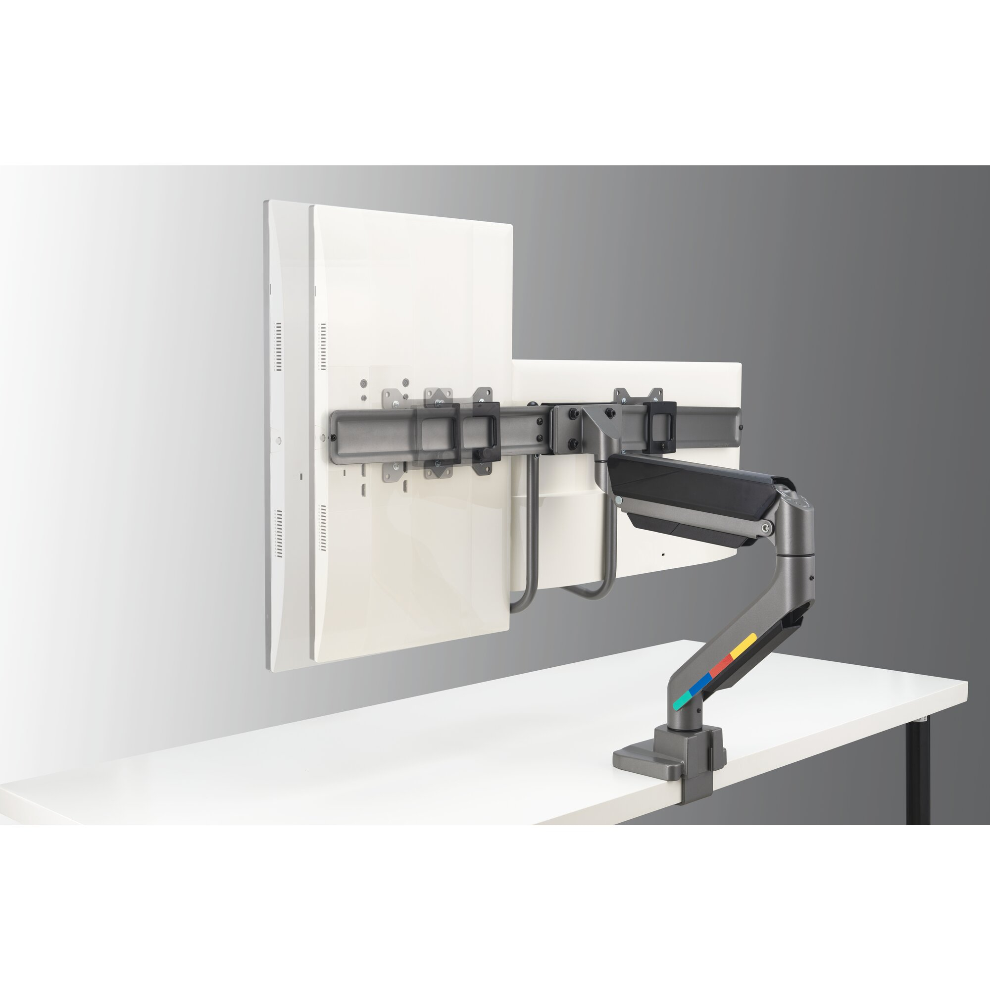 A gray monitor arm with colorful accents holds a white monitor on a white desk.