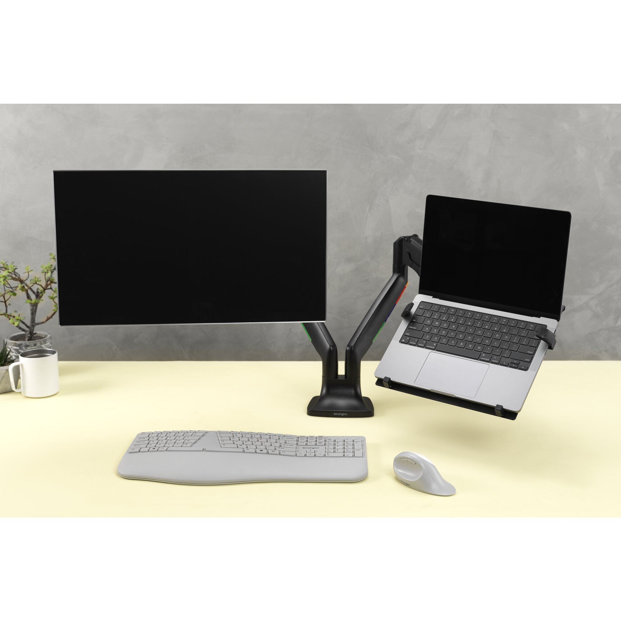 A desk with dual monitors, keyboard, and mouse against a concrete wall.