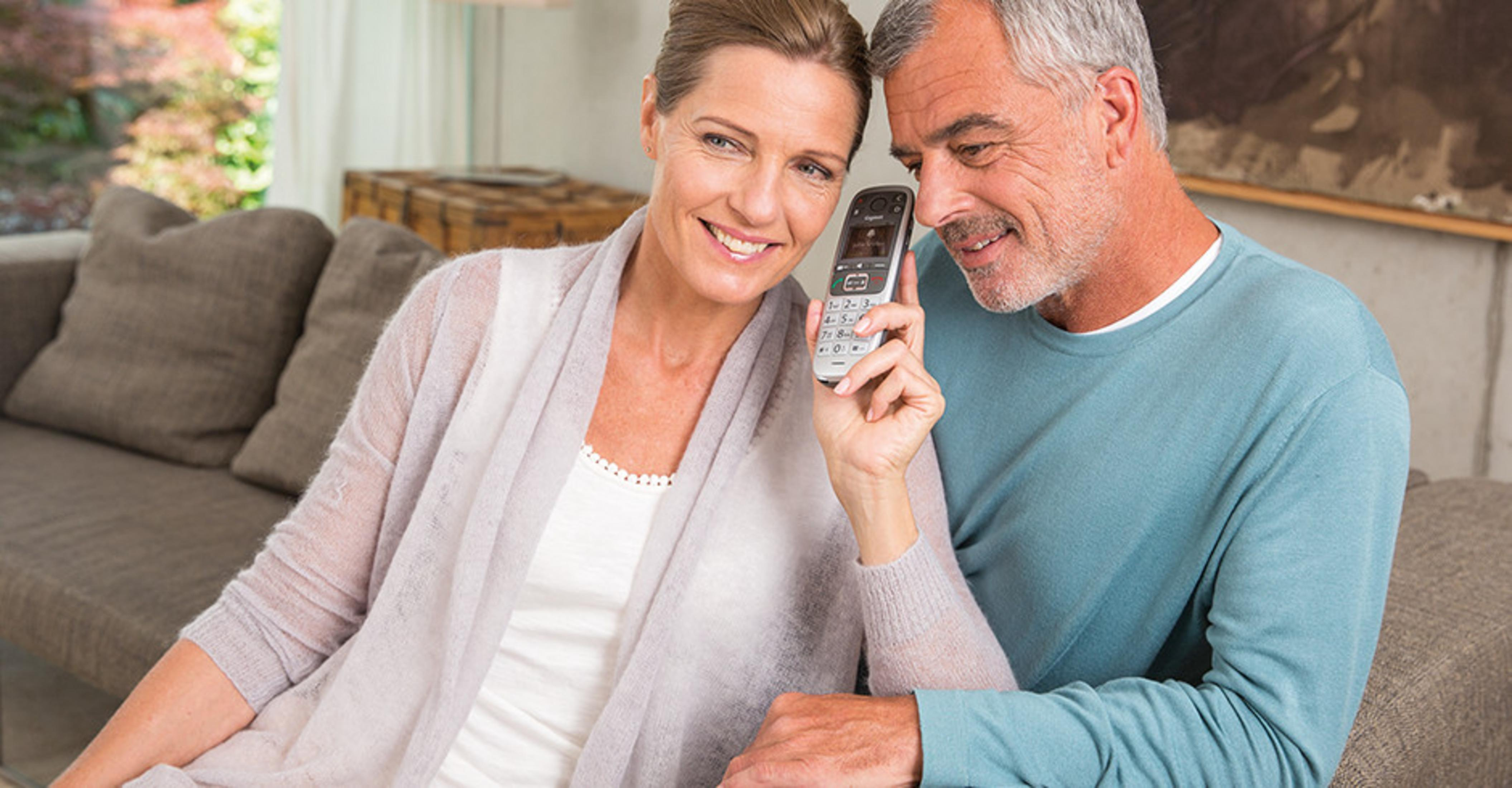 Un uomo e una donna siedono su un divano, tenendo un telefono cordless.