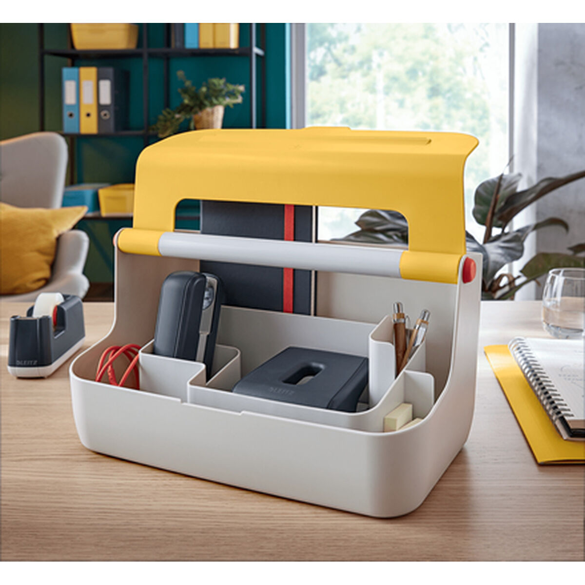 Ein gelber und weißer Schreibtischorganizer mit Hefter, Klebebandabroller, Stiften und Notizbüchern.
