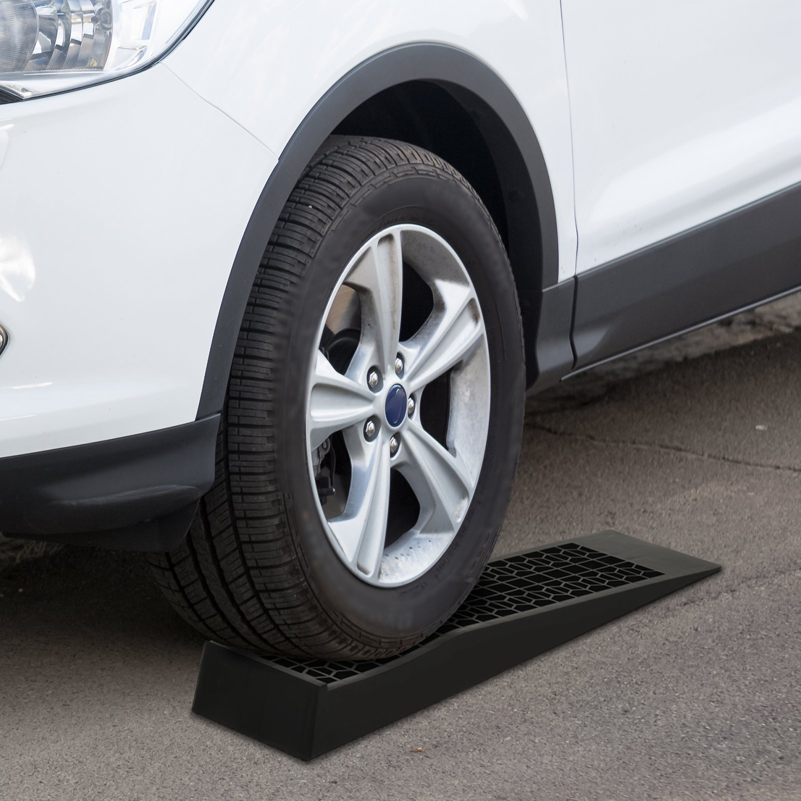 Una rampa negra para autos debajo de la rueda de un auto blanco sobre asfalto.