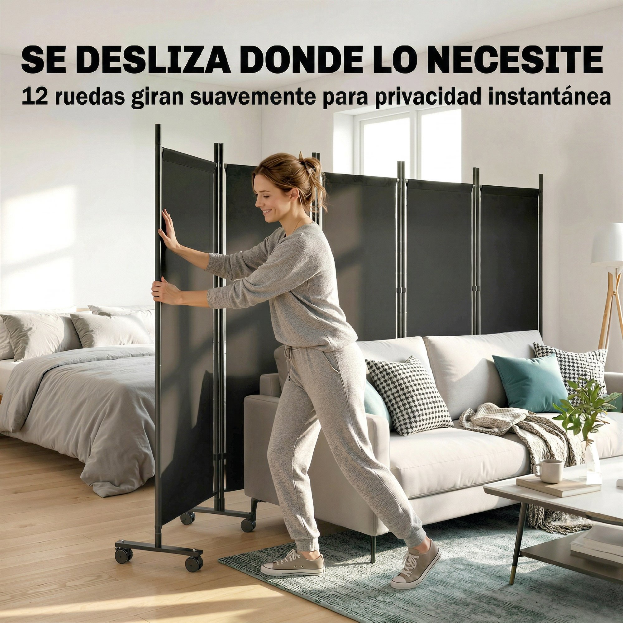 Mujer empuja un divisor de habitación negro con ruedas junto a una cama y sofá.