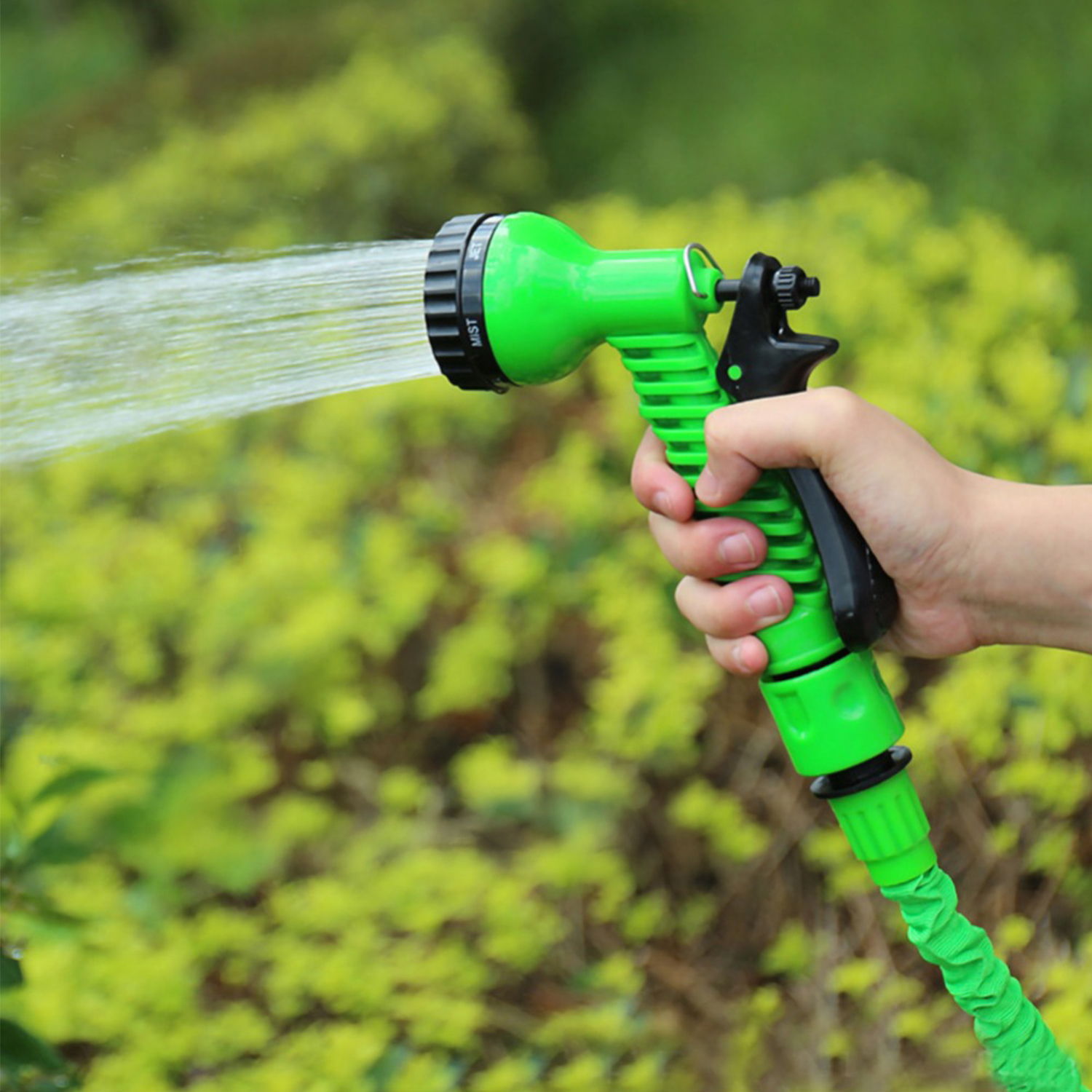 Una boquilla de manguera verde rocía agua frente a un follaje verde exuberante.