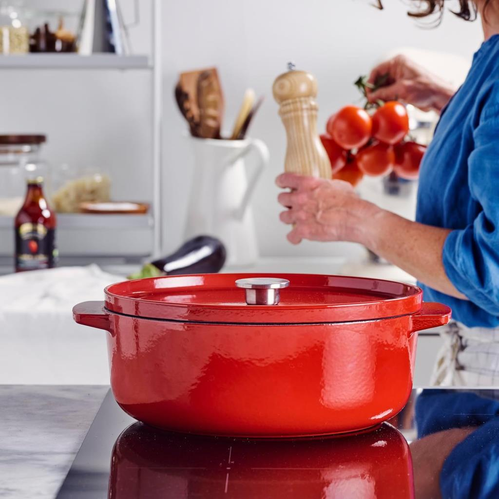 Mavi gömlekli bir kişi kırmızı tencere ve domateslerle yemek yapıyor.
