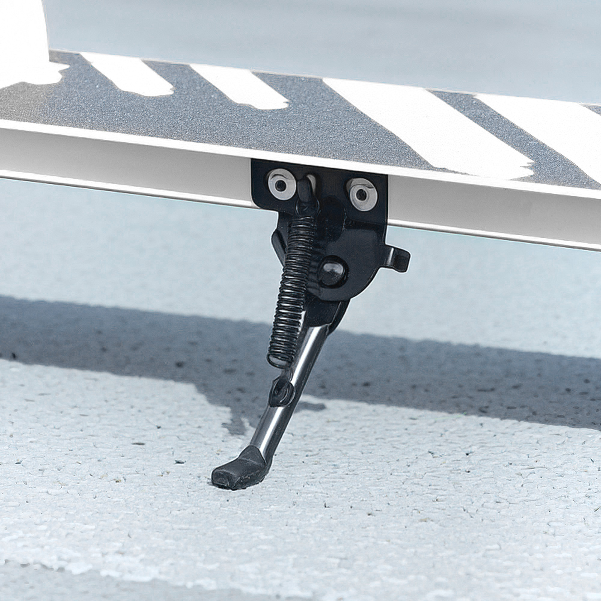 Un caballete negro está sujeto a un patinete, apoyado en asfalto gris.