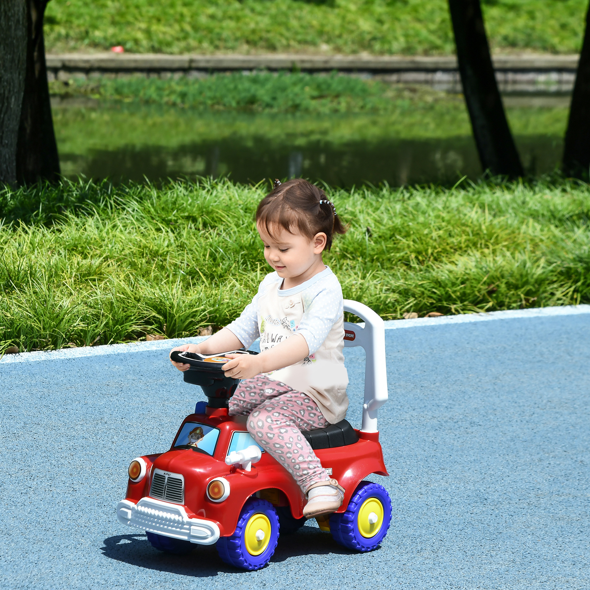 Una niña pequeña conduce un coche de juguete rojo en un camino azul en un parque.