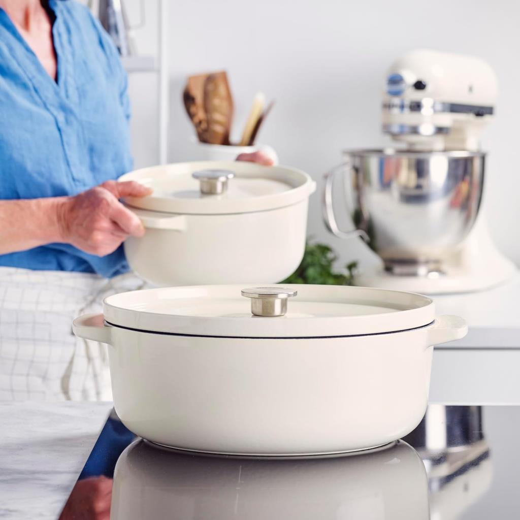 Eine Person hält einen weißen Topf. Ein weiterer weißer Topf und ein Mixer sind in der Nähe.
