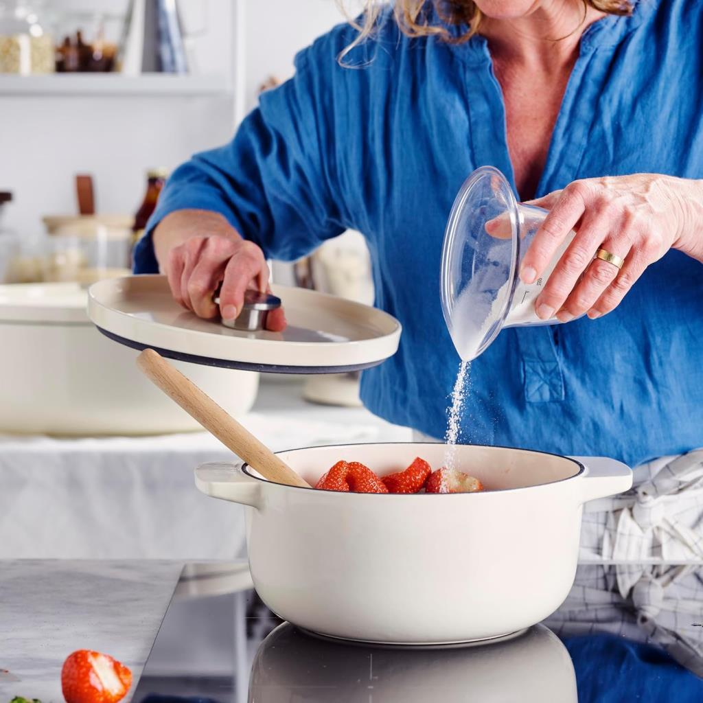 Person in blauem Hemd gibt Zucker in Topf mit Erdbeeren. Deckel in linker Hand gehalten.