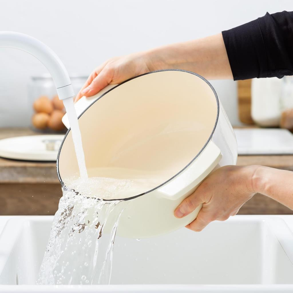 Eine weiße Kochtopf wird über einer Spüle geleert, Wasser fließt aus dem Topf.