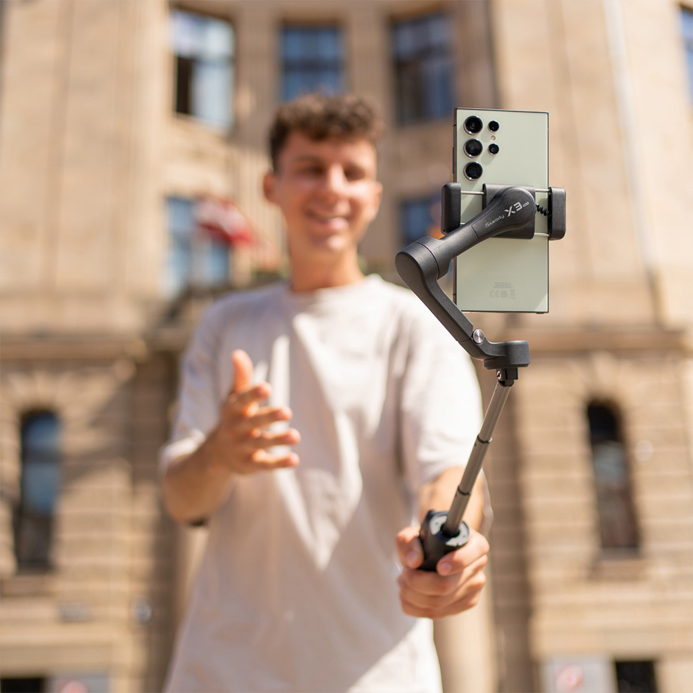 Un hombre sostiene un gimbal con un smartphone verde claro hacia la cámara.