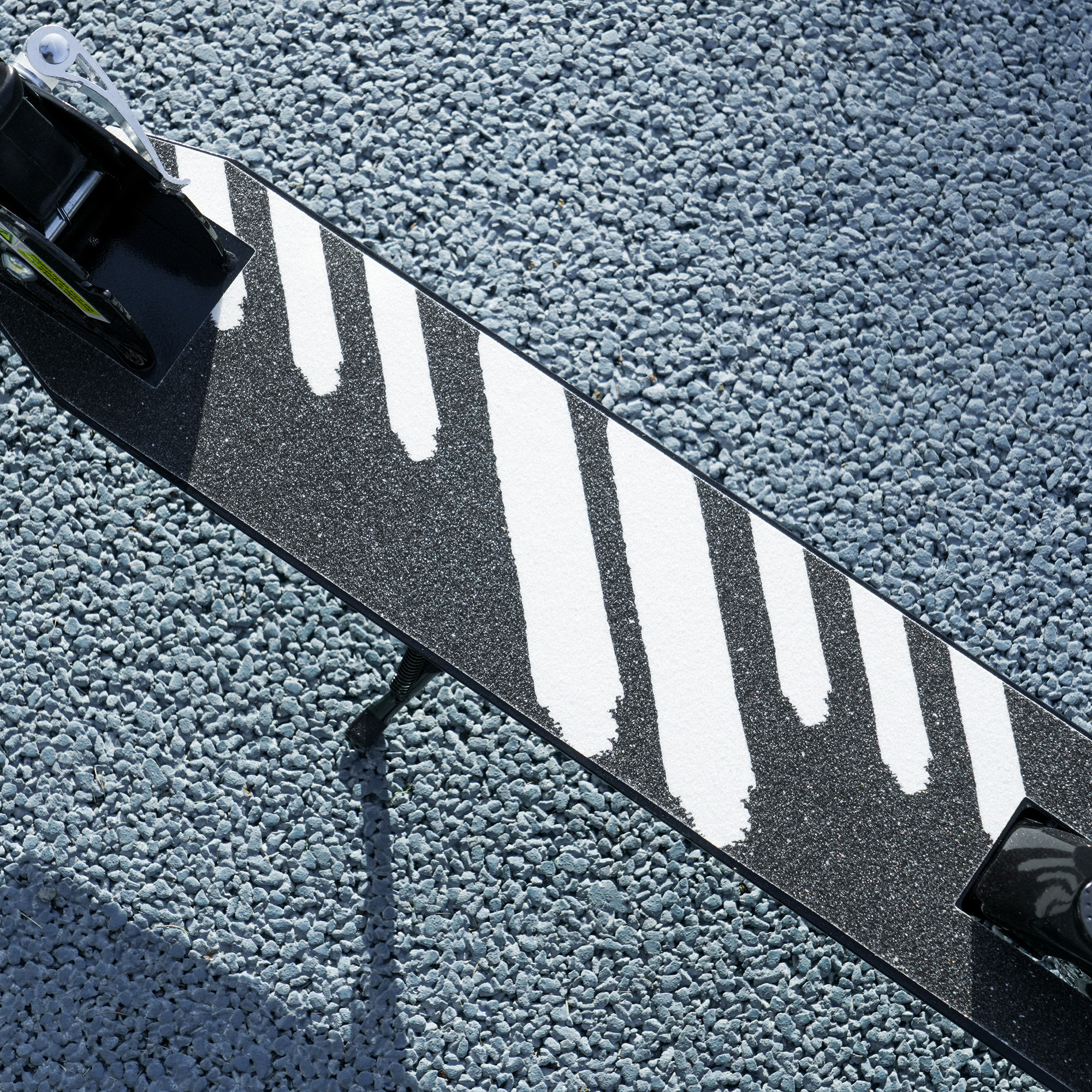 Primer plano de un patinete sobre grava. Tabla negra con rayas blancas.
