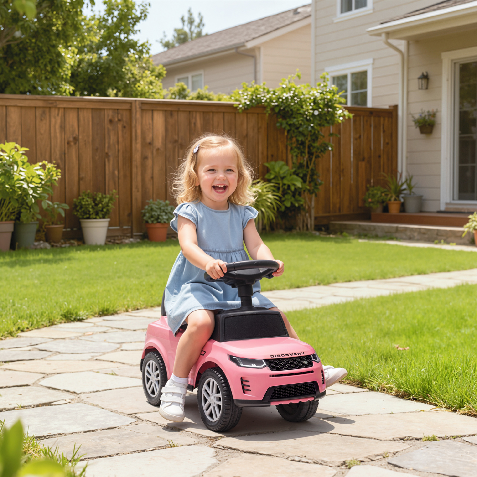 Una niña pequeña con vestido azul monta un coche de juguete rosa en un camino de piedra.