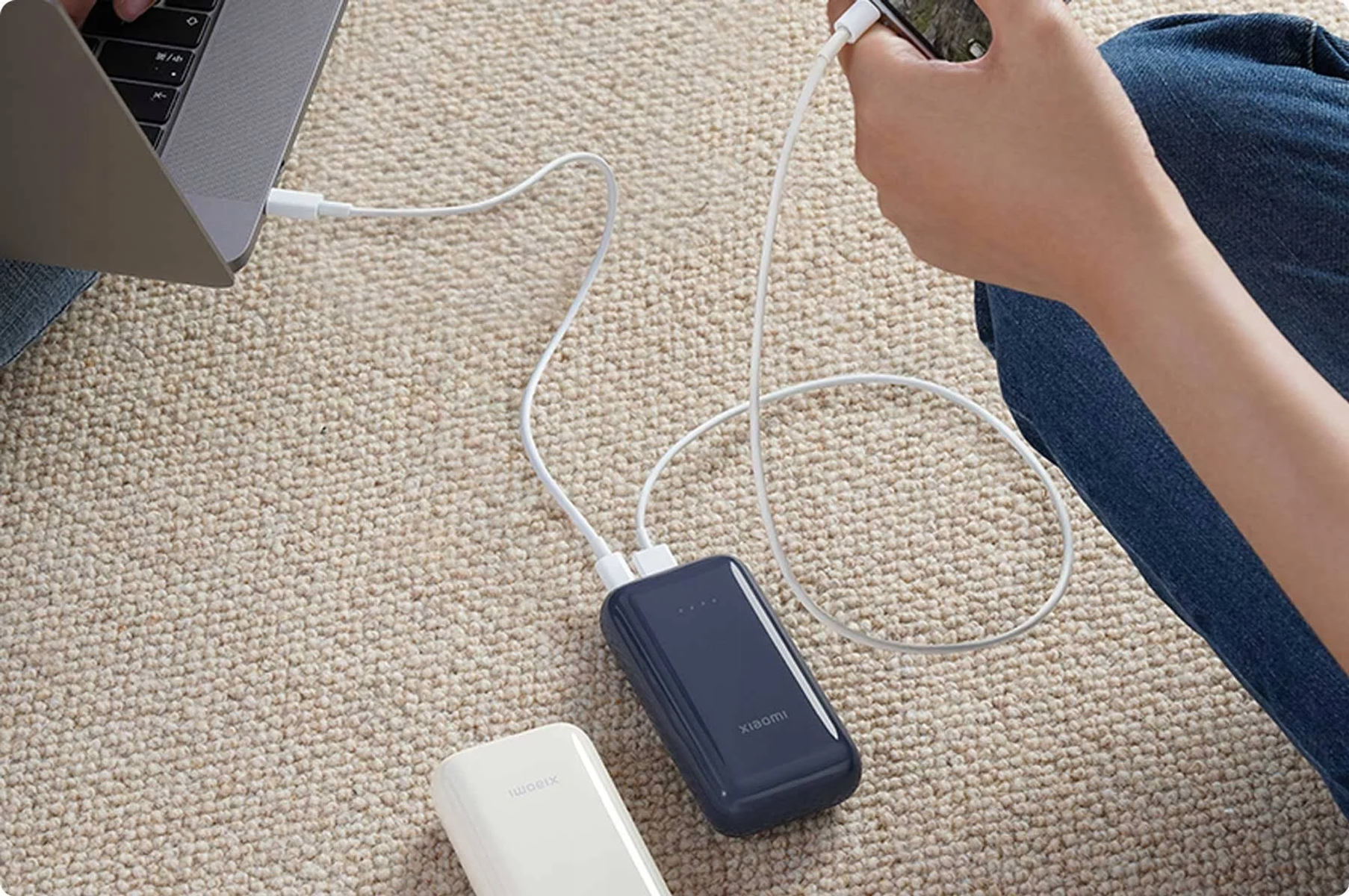 Ciemnoniebieski power bank Xiaomi ładuje telefon, obok biały power bank.