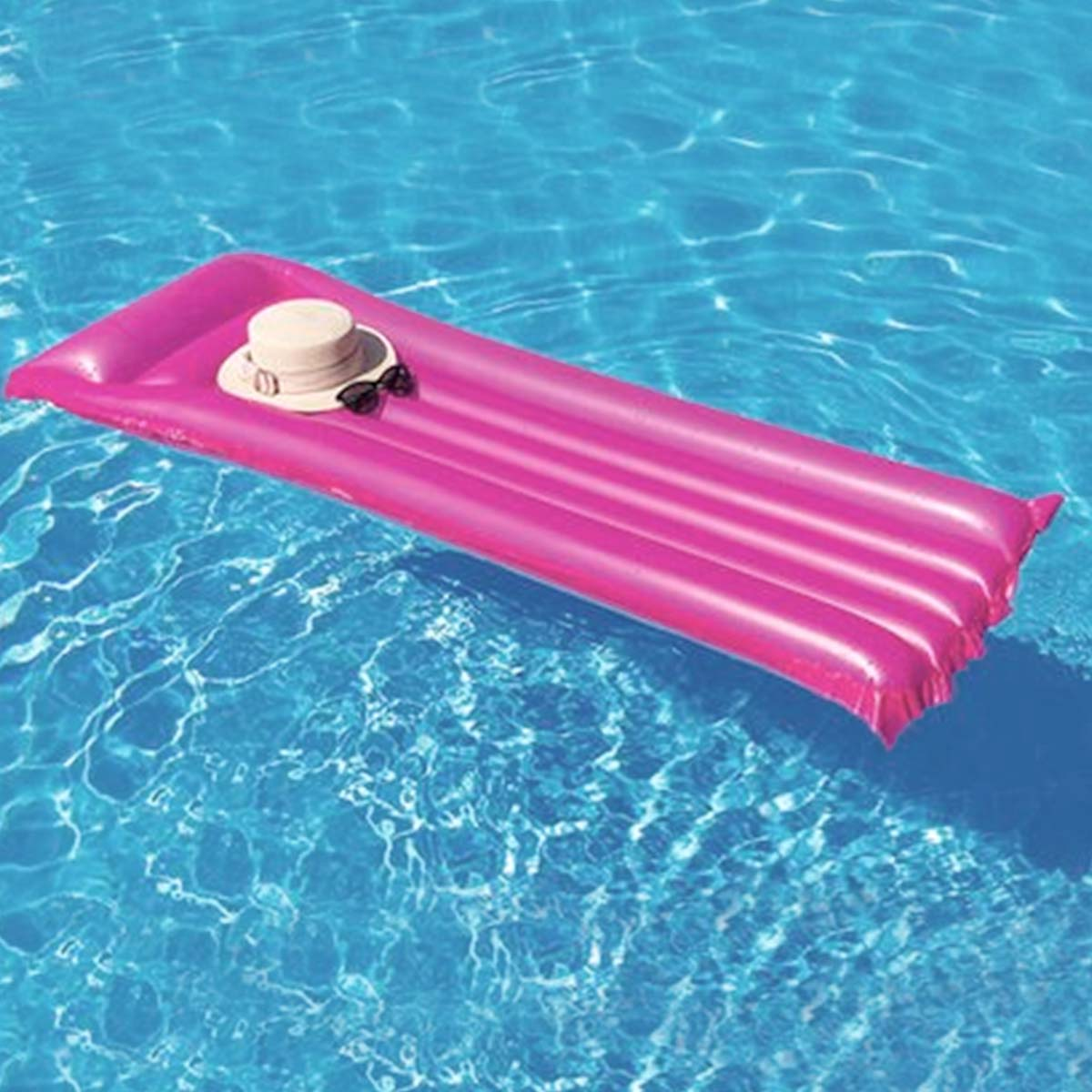 Un vivace materassino gonfiabile rosa galleggia su acqua azzurra e limpida. Un cappello chiaro e occhiali da sole riposano su di esso.