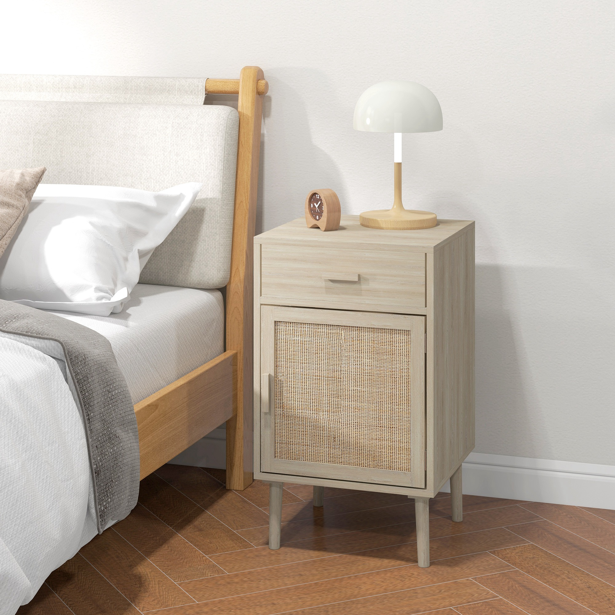 Una mesita de noche de madera clara con puerta de ratán junto a una cama con sábanas blancas.