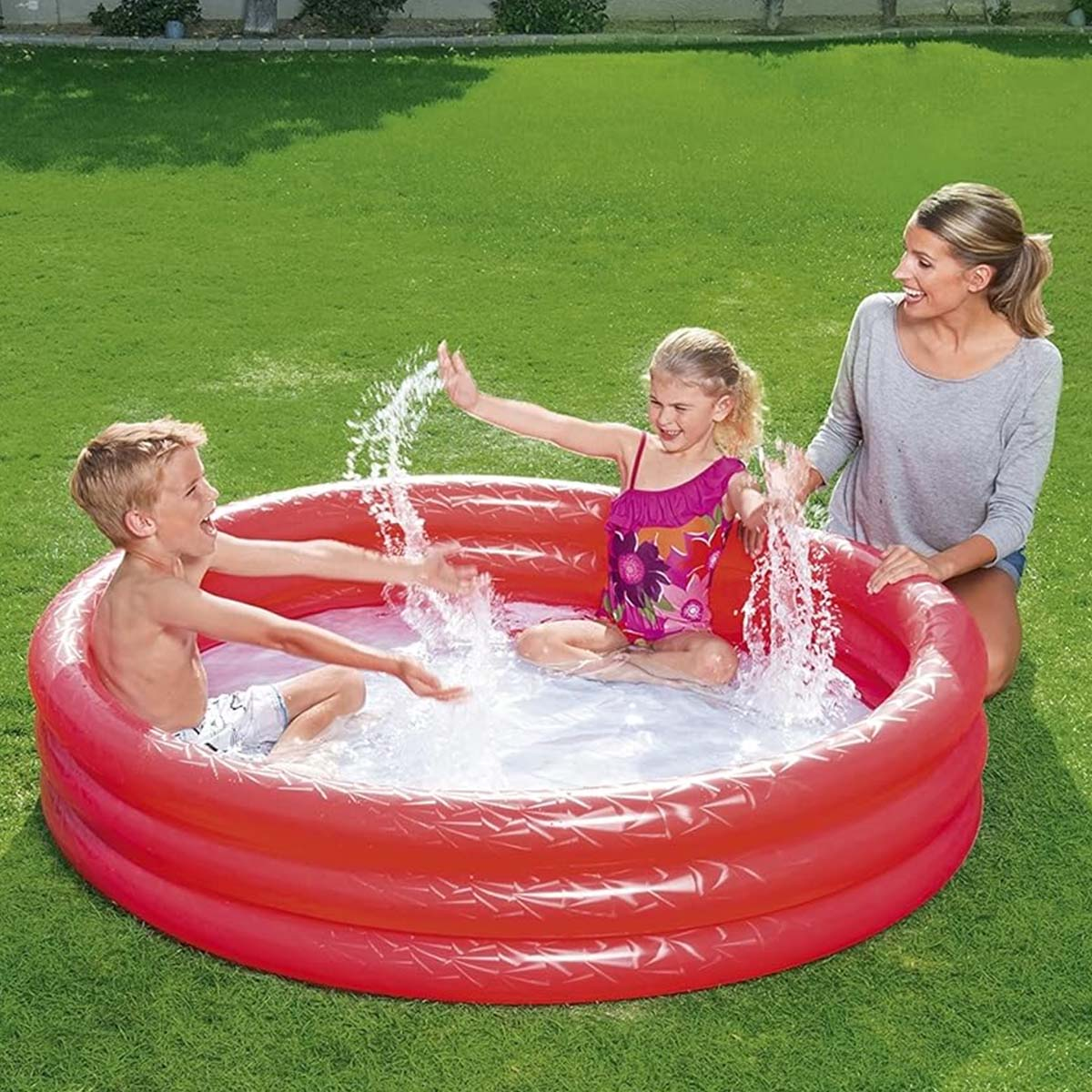 Bambino e bambina schizzano nella piscina rossa, una donna guarda.