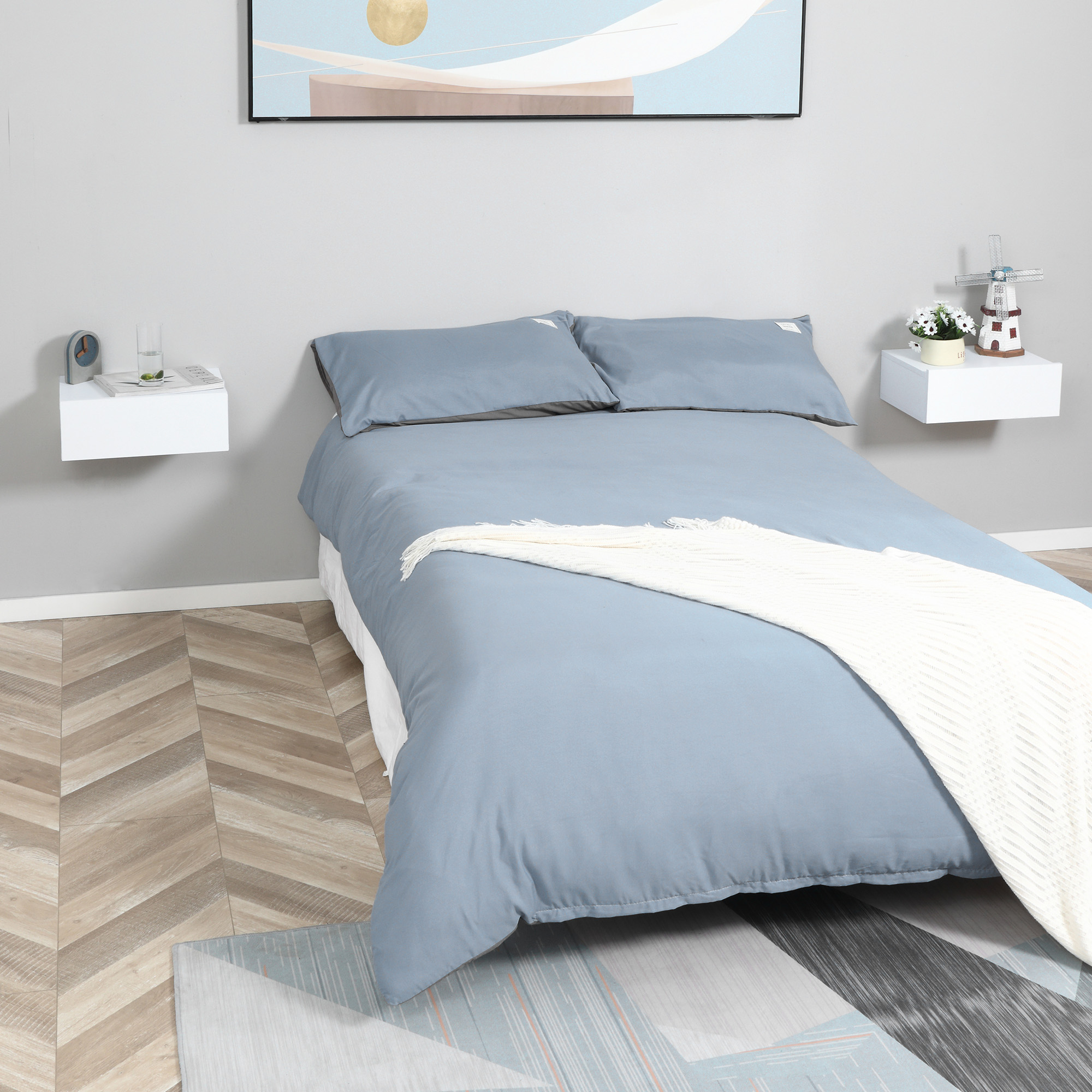 Una cama azul con almohadas blancas y manta, junto a mesitas de noche flotantes.