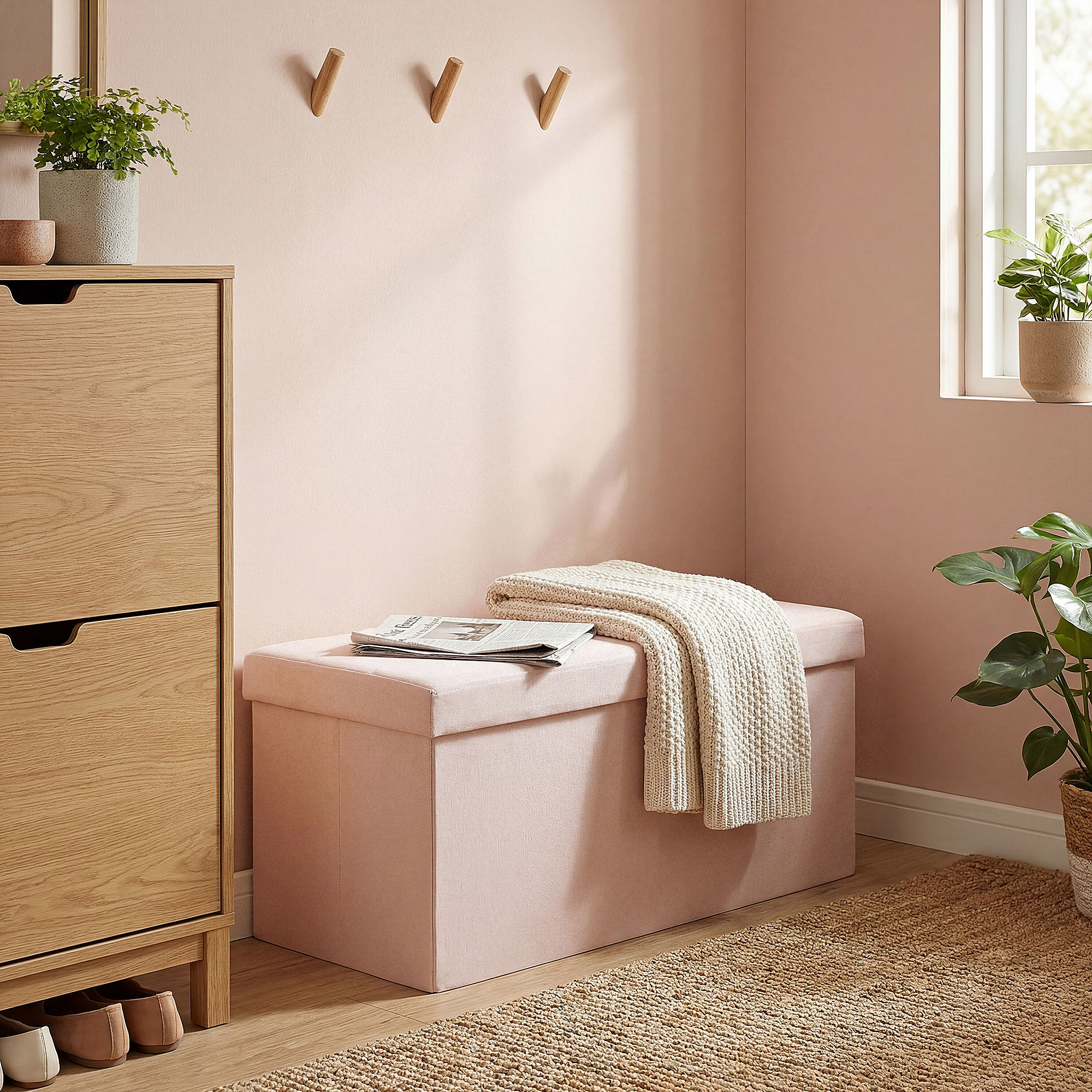 Un banco de almacenamiento rosa con manta y periódico junto a un zapatero de madera.