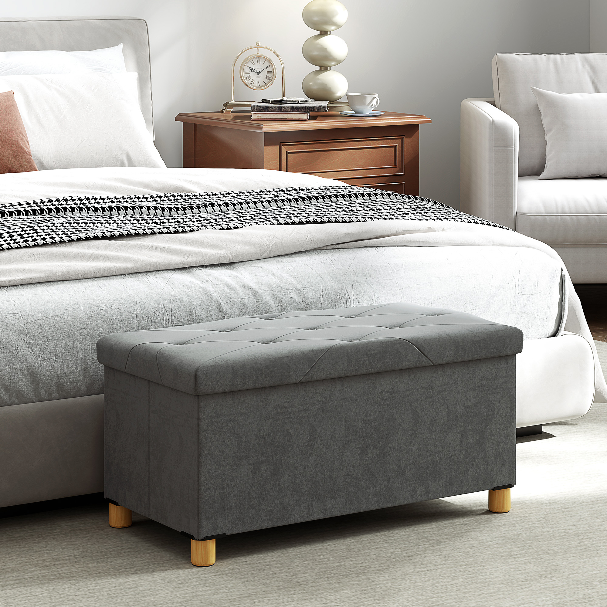 Banqueta gris con capitoné y patas de madera delante de una cama.