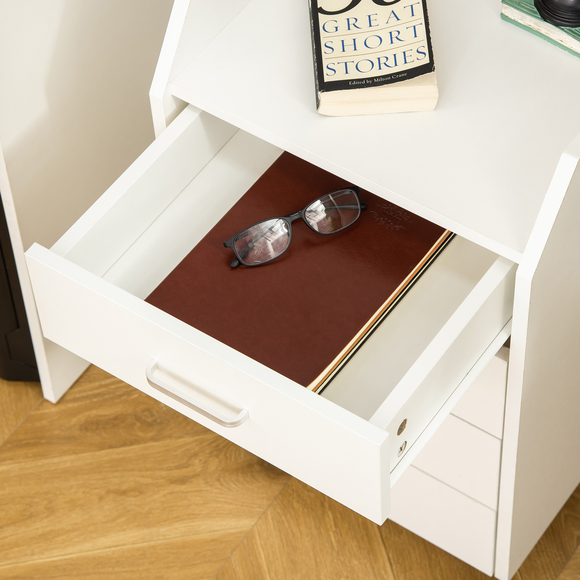 Un cajón blanco abierto con un libro marrón y gafas dentro.