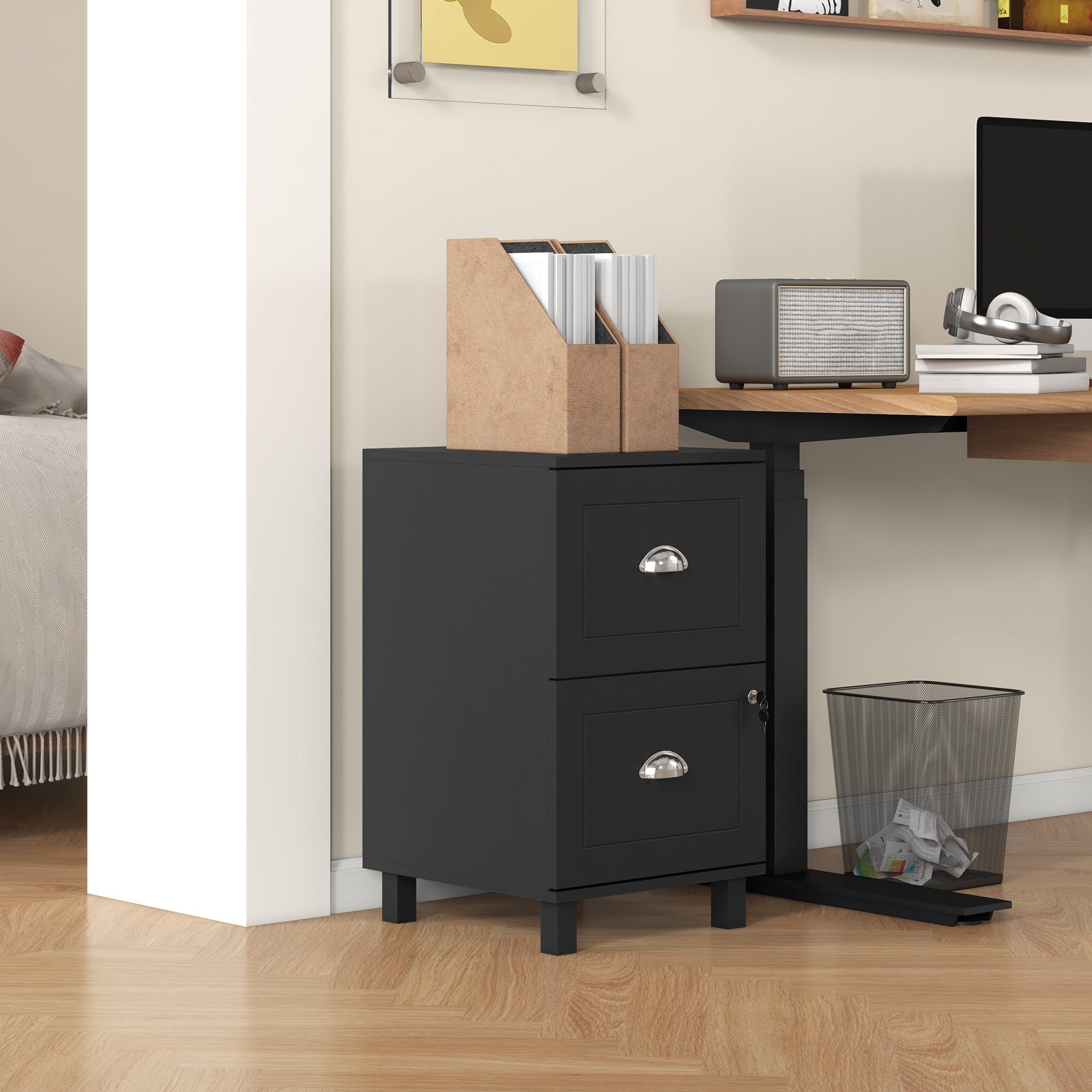 Gabinete de archivo negro con dos cajones, junto a una papelera de malla. Escritorio con computadora.