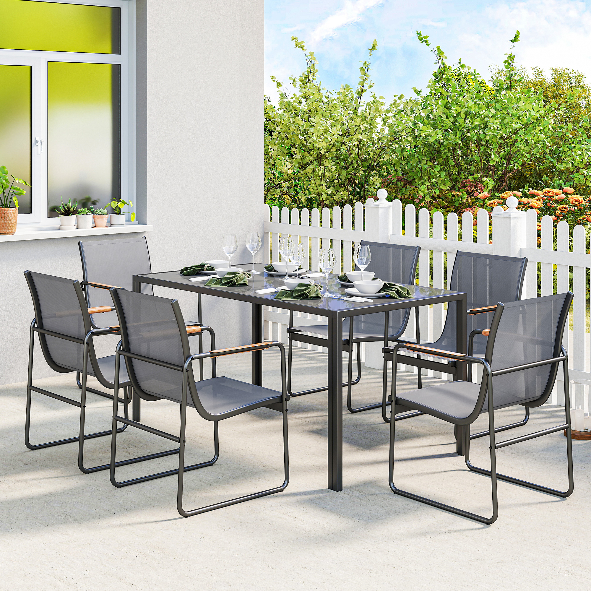 Una mesa de comedor gris con seis sillas en un patio con valla blanca y plantas.