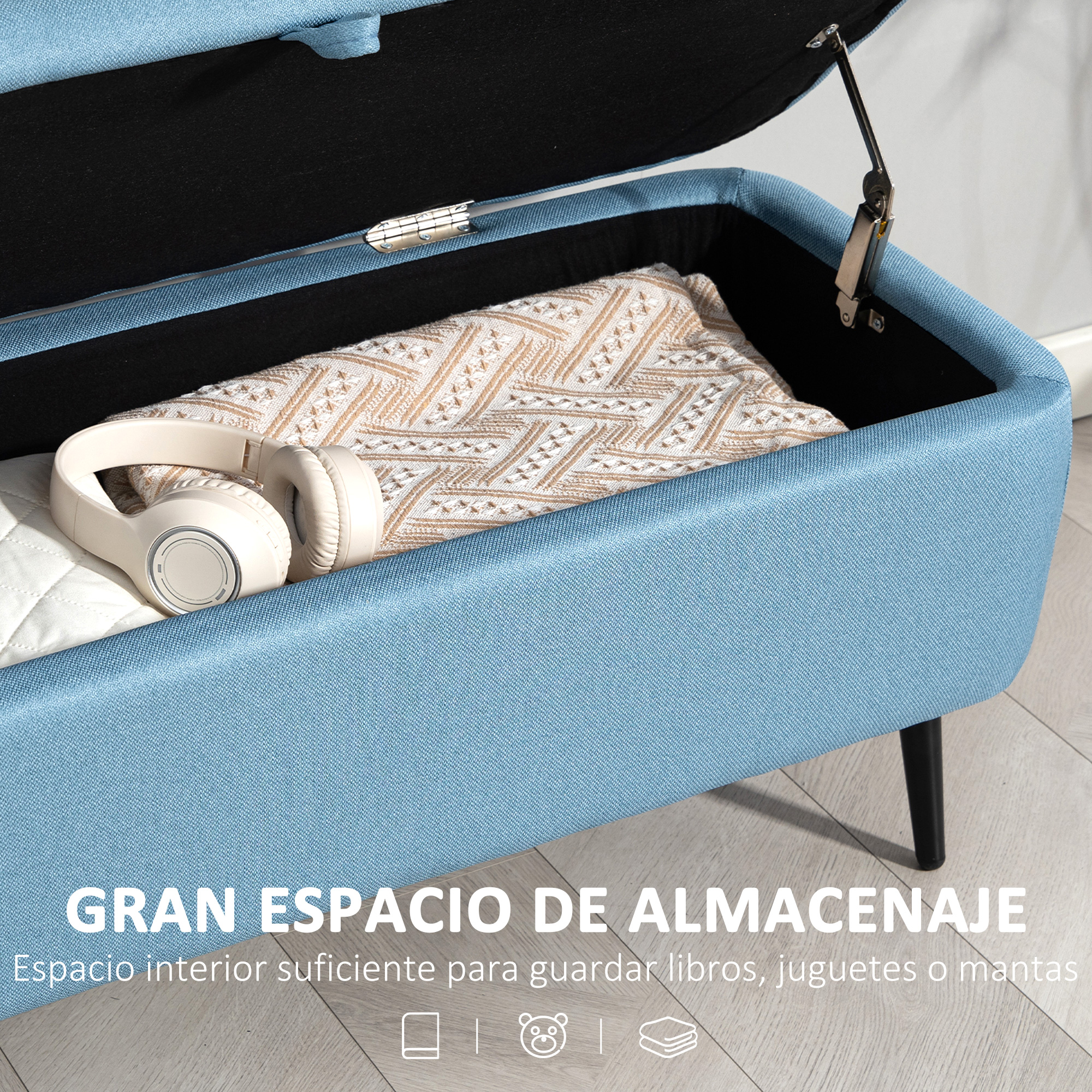Un otomana de almacenamiento azul claro con tapa abierta, con auriculares y manta dentro.