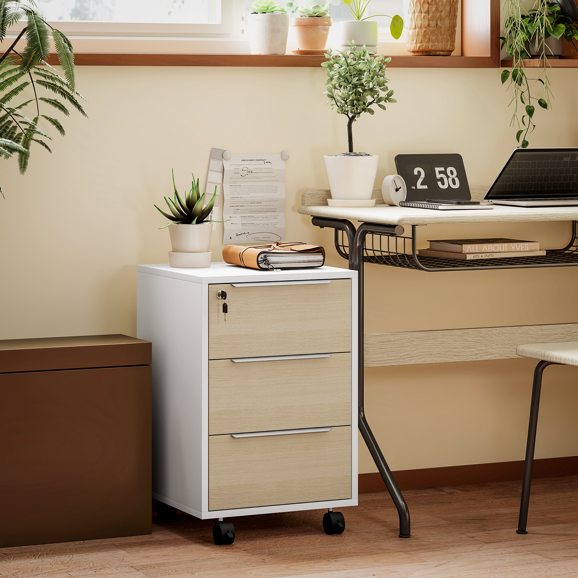 Un escritorio con plantas, archivos y un portátil, al lado de un archivador blanco con ruedas.