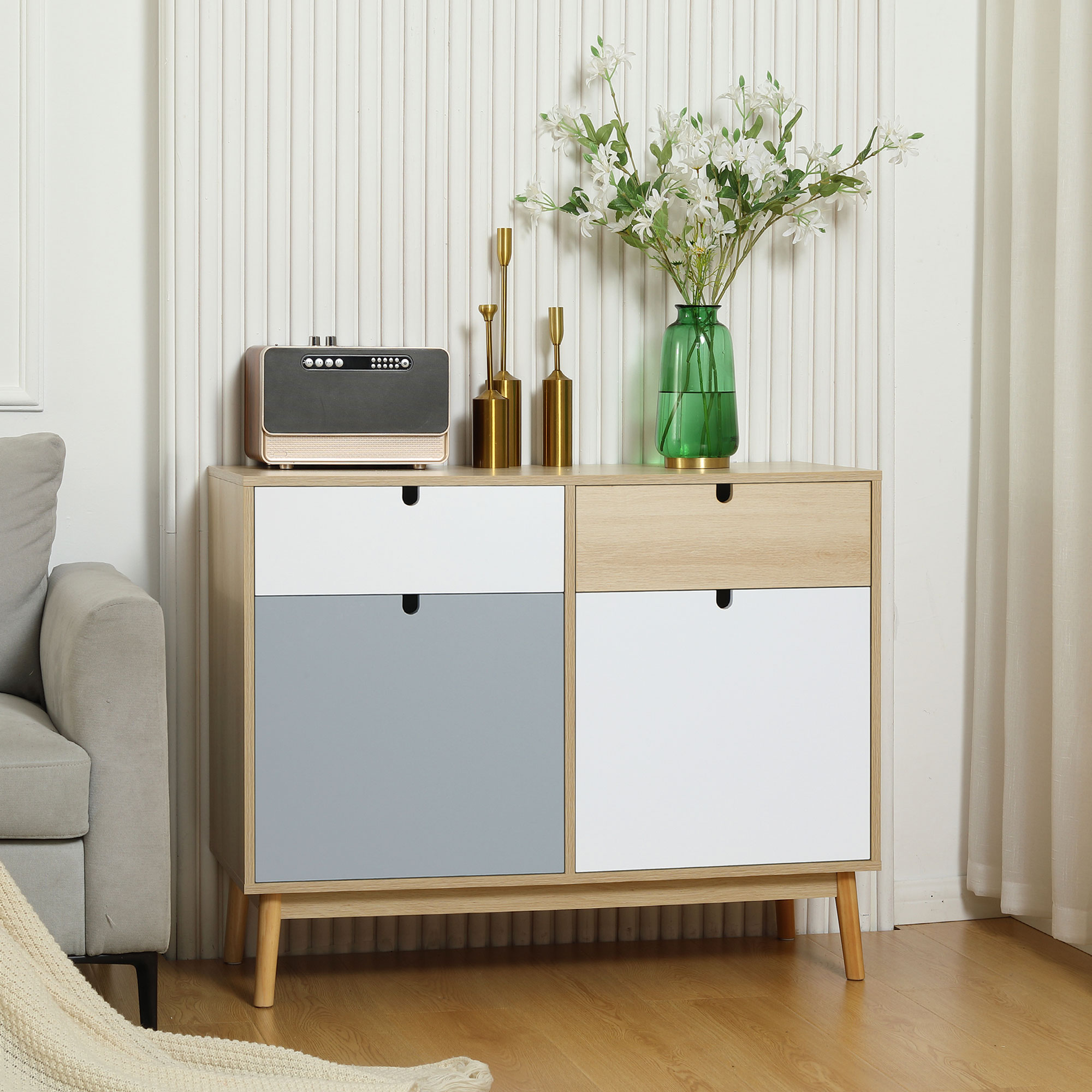 Mueble de madera con cajones blancos y grises, con radio, candelabros y jarrón con flores encima.