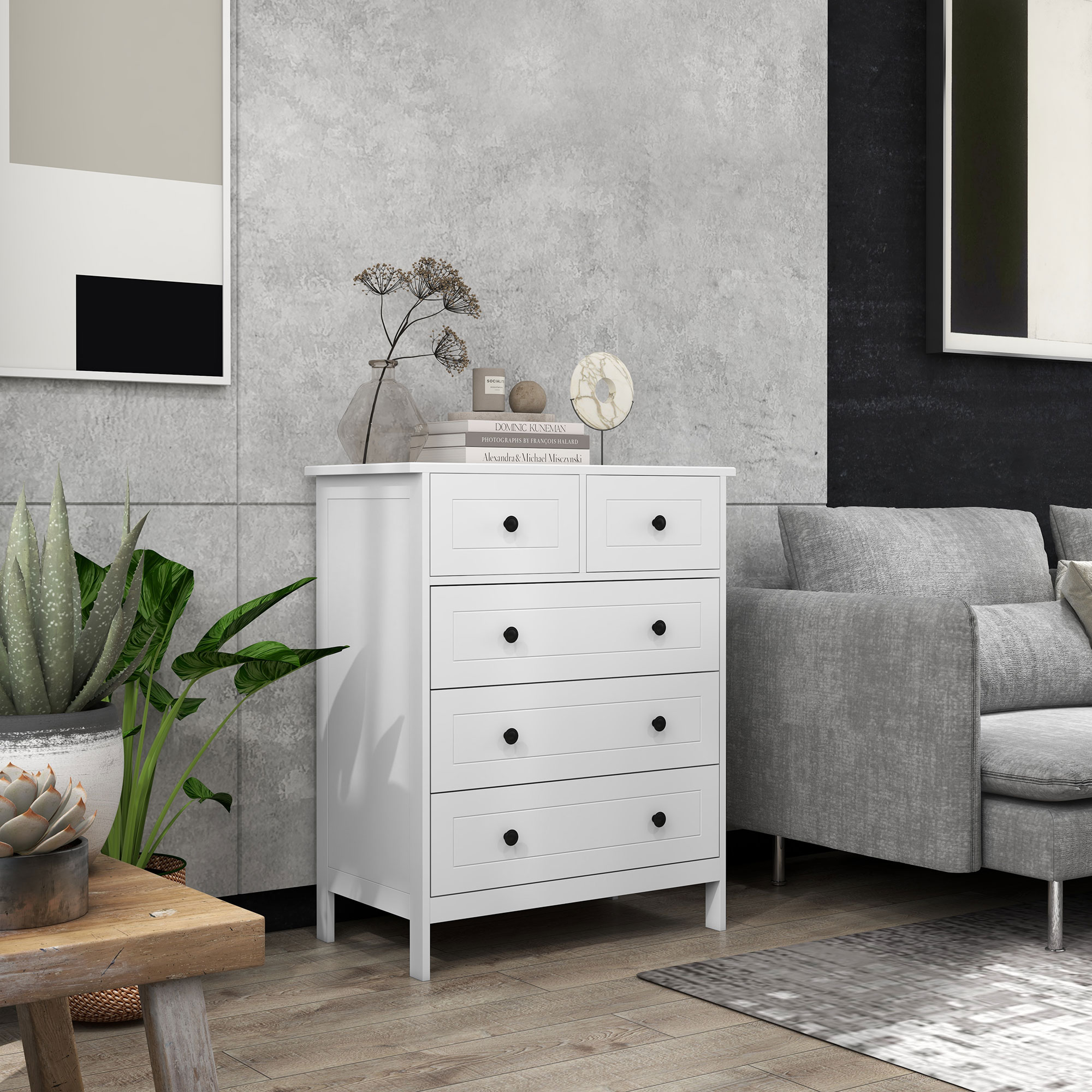 Una cómoda blanca con pomos negros junto a un sofá gris. Hay plantas a la izquierda.