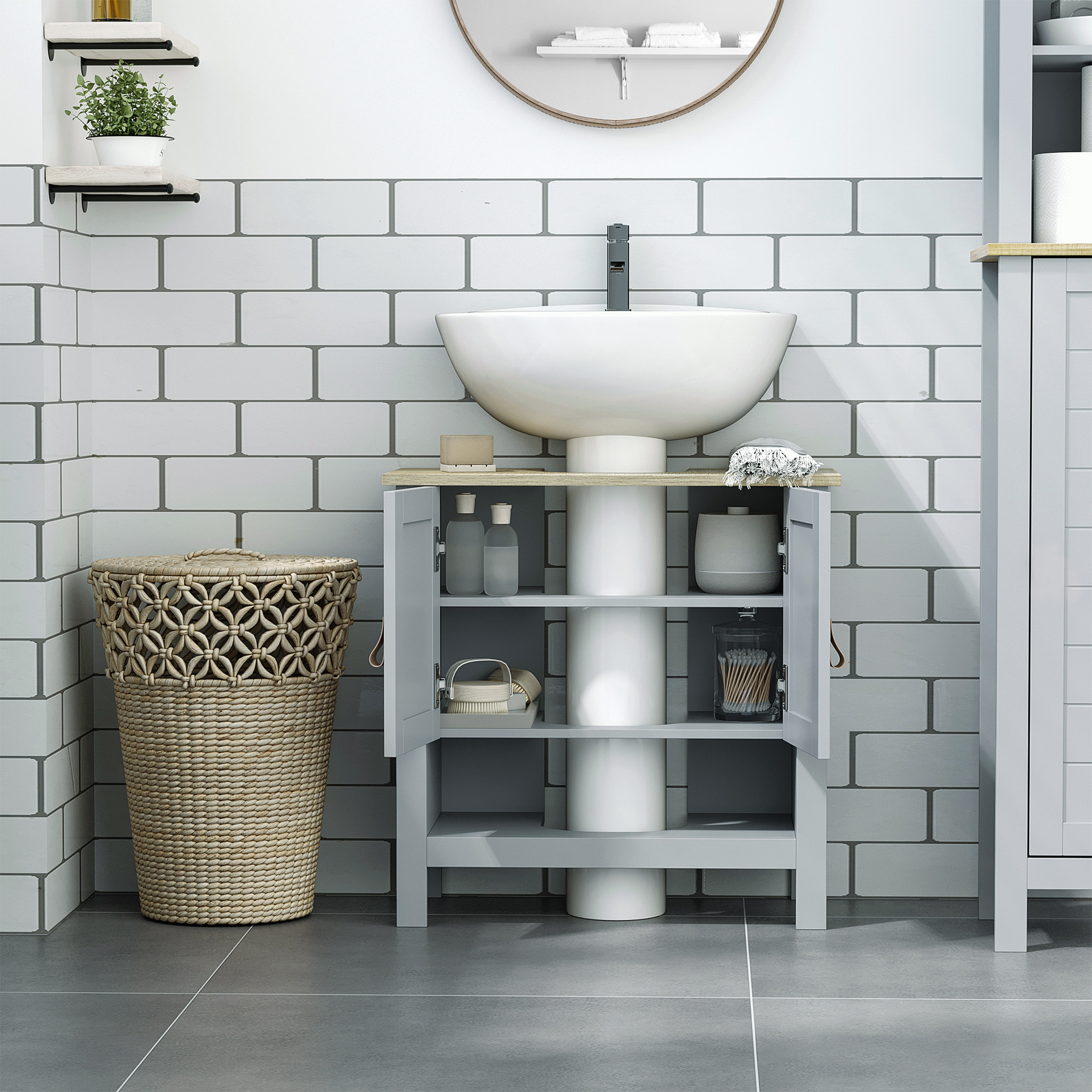Un baño con lavabo sobre encimera, mueble de tocador gris, espejo redondo y cesta tejida.