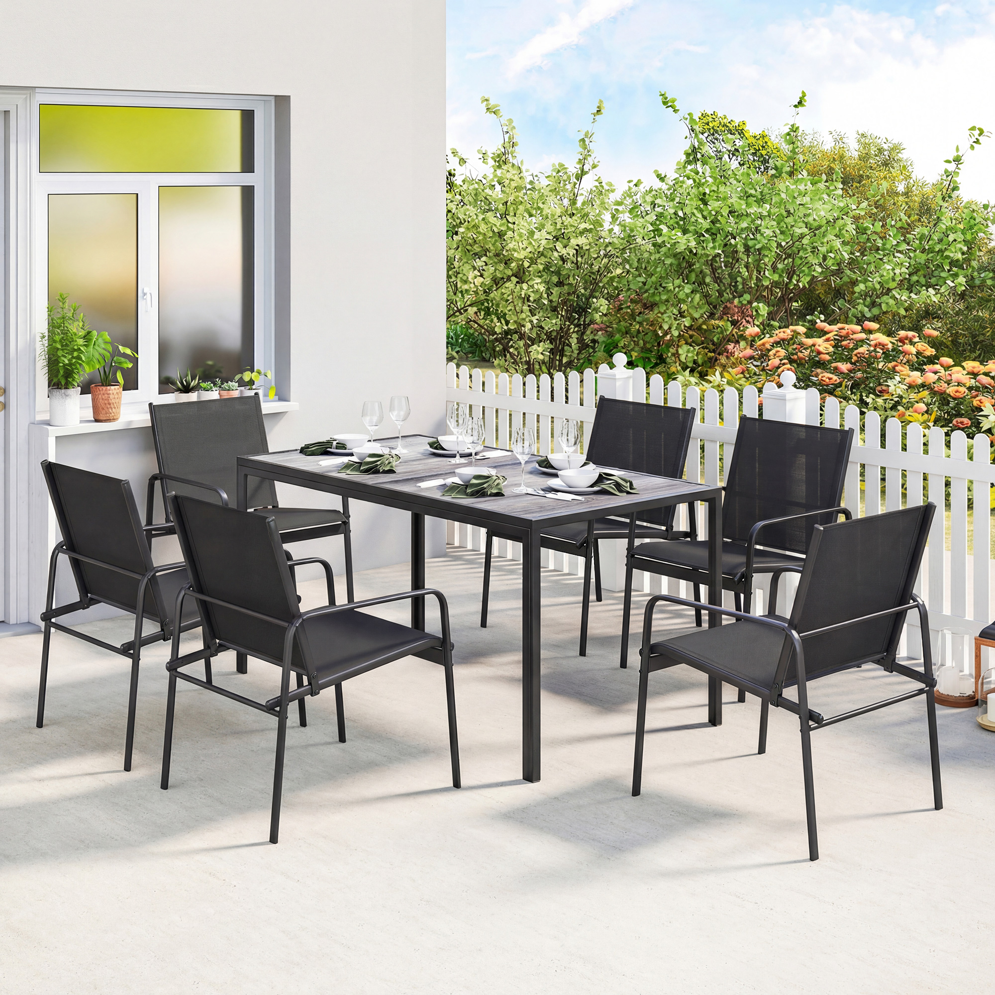 Un tavolo da pranzo grigio con sedie su un patio, con piante e una recinzione sullo sfondo.