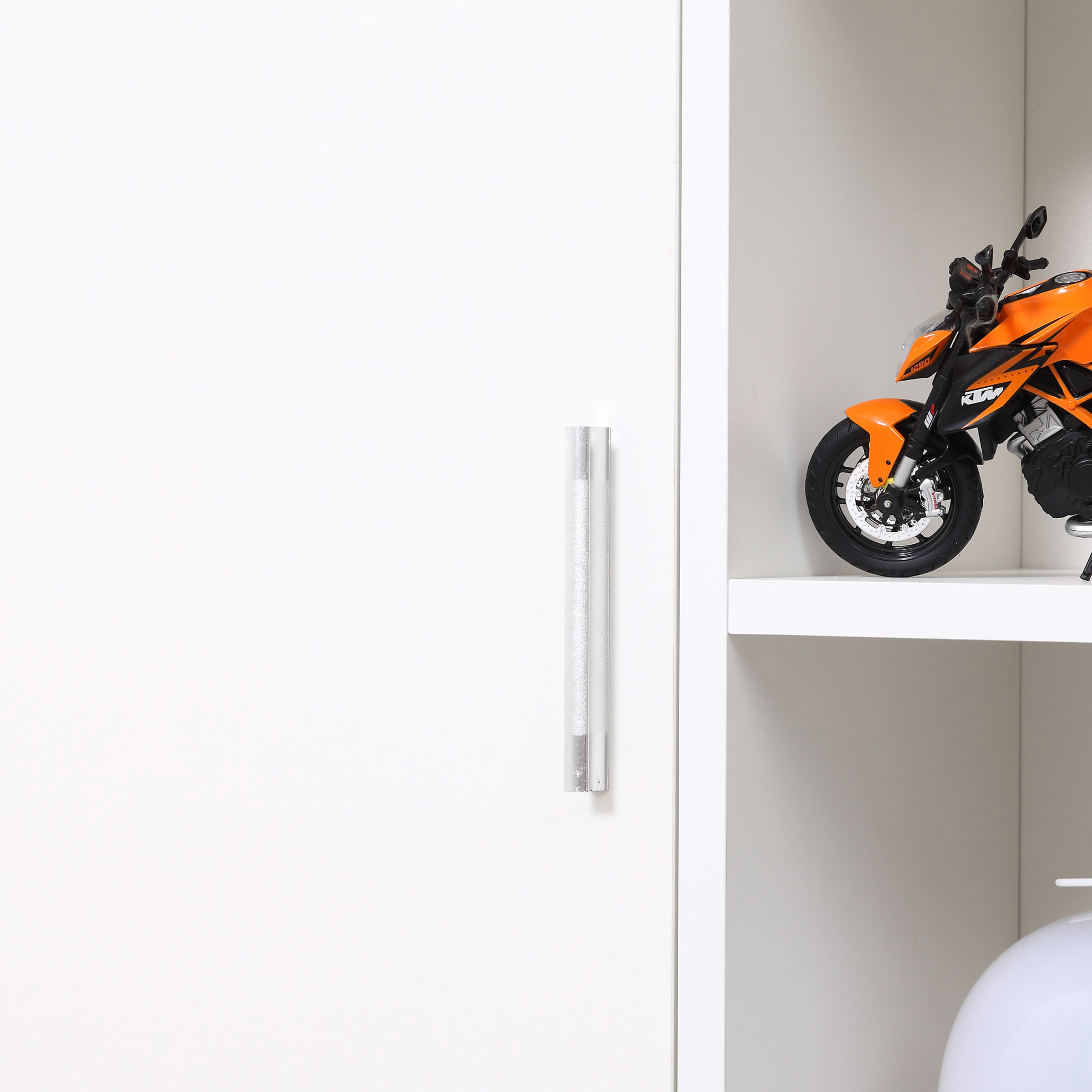 Una motocicleta de juguete naranja se sienta en un estante blanco junto a un armario blanco.