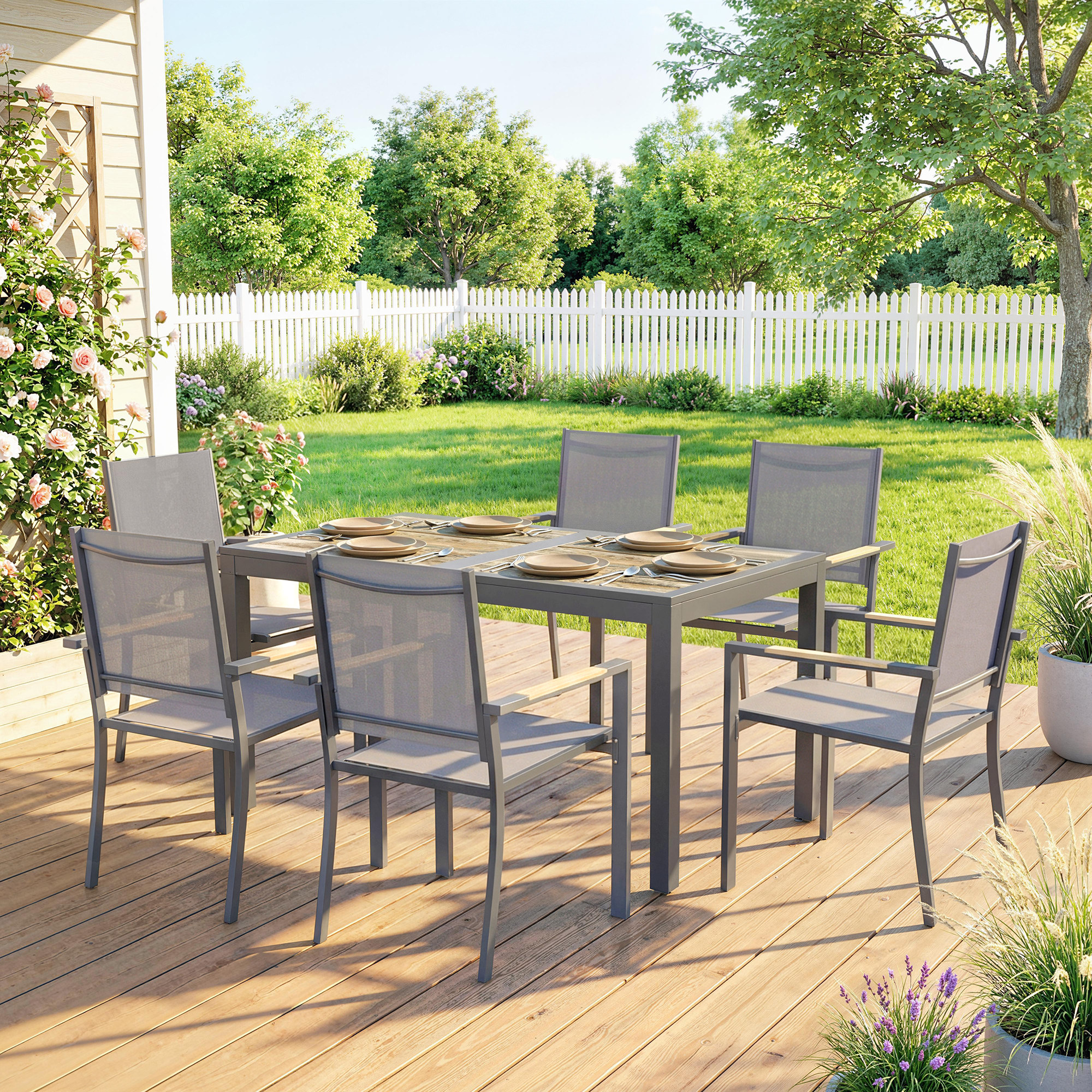 Una mesa de comedor de metal con seis sillas en una terraza de madera, en un jardín con valla.
