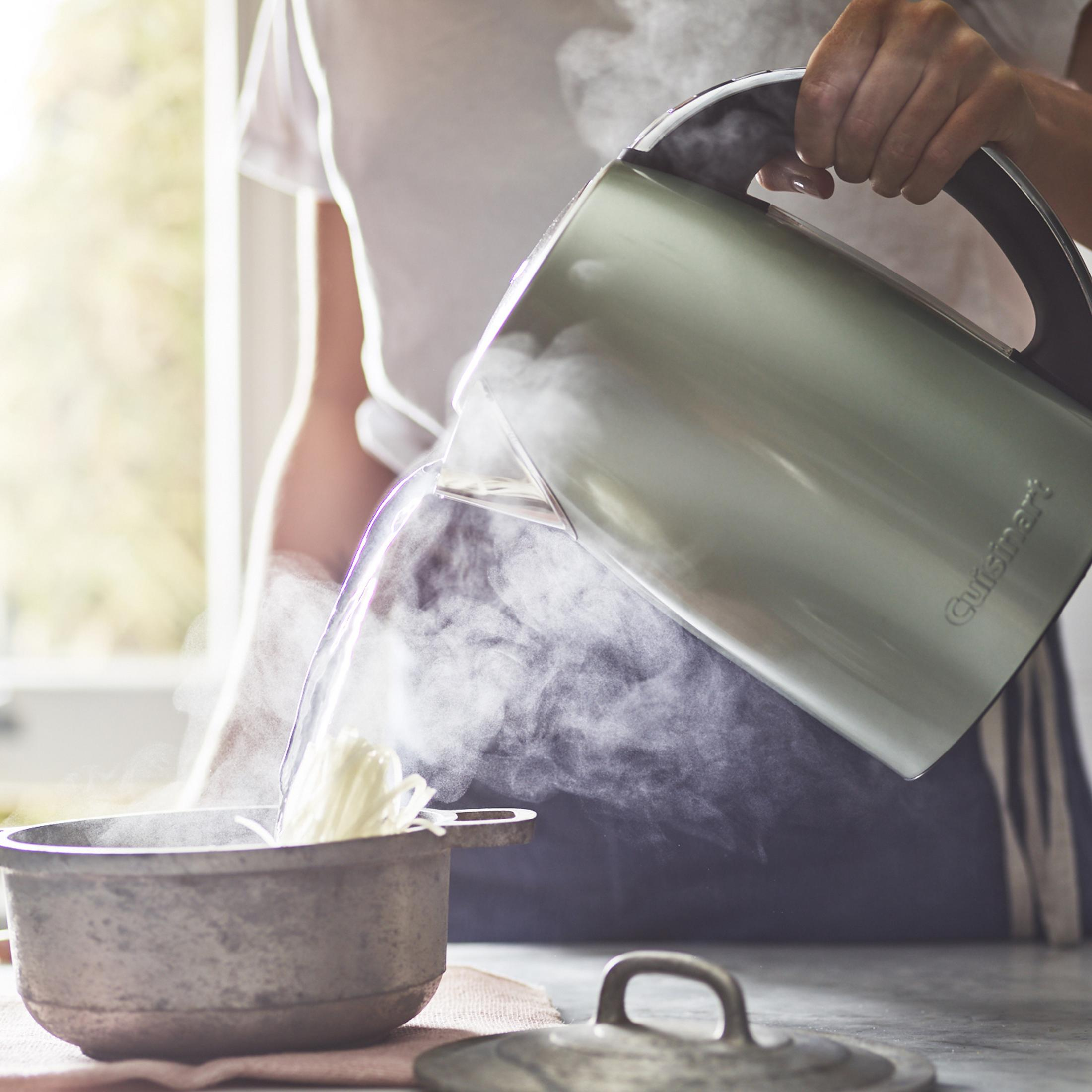Una persona versa acqua calda da un bollitore in una pentola di noodles.