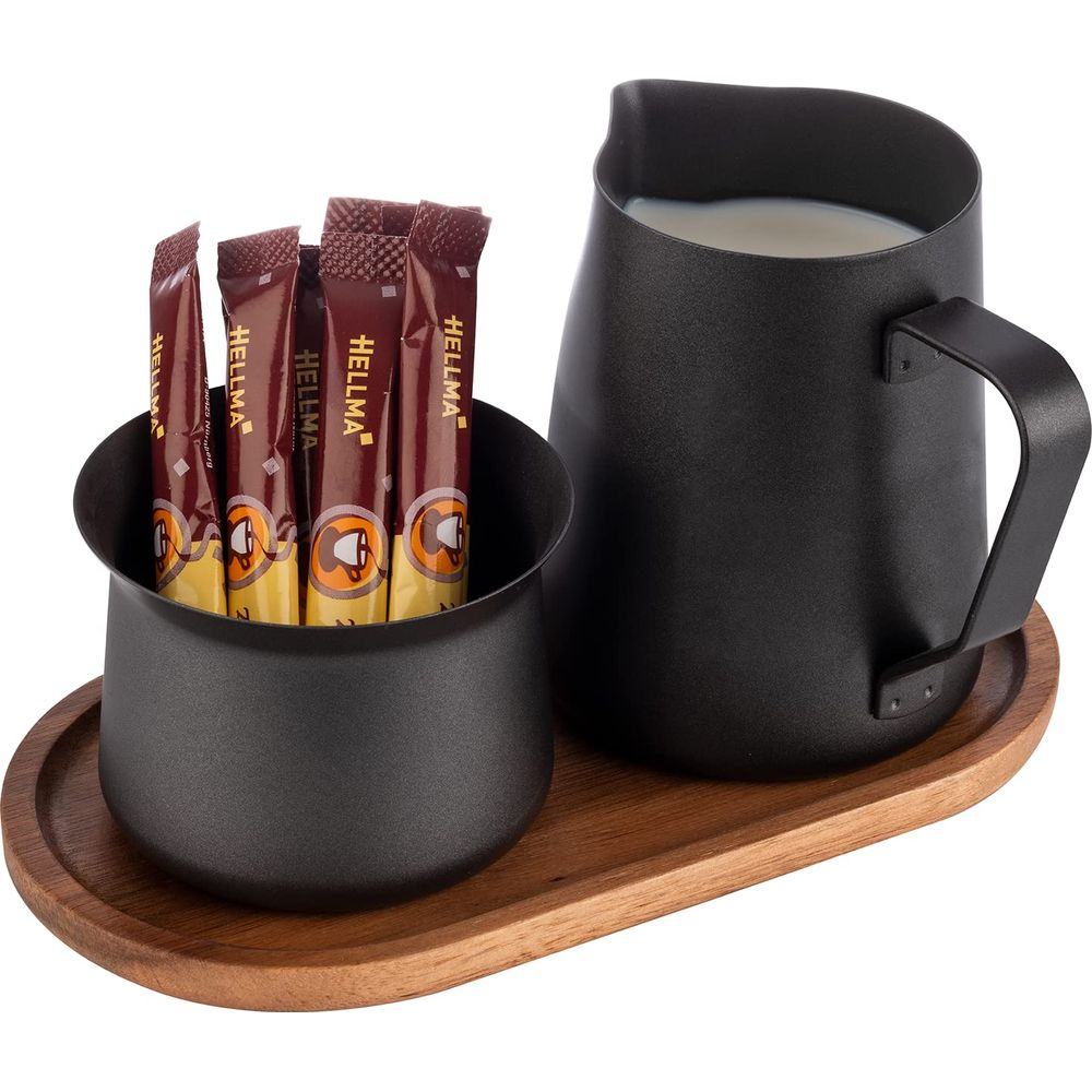 Schwarzer Milchaufschäumer und Behälter mit vier Kaffeepackungen auf Holztablett.