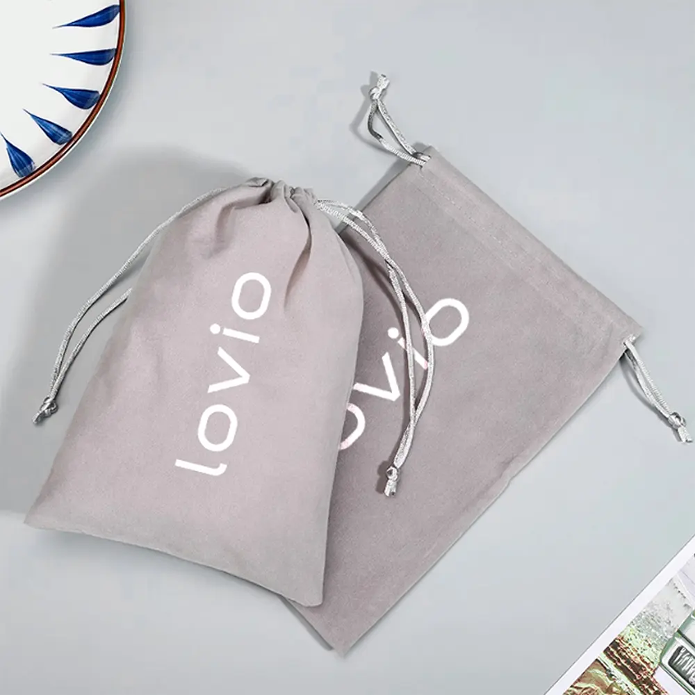 Dwa szare worki na sznurki z logo 'lovio' na szarej powierzchni, obok talerza.