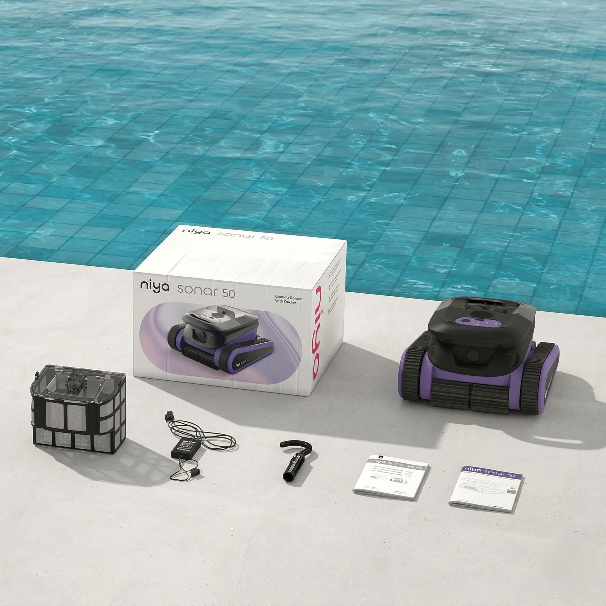 Un limpiador de piscina morado y negro, su caja y accesorios en la terraza de una piscina.