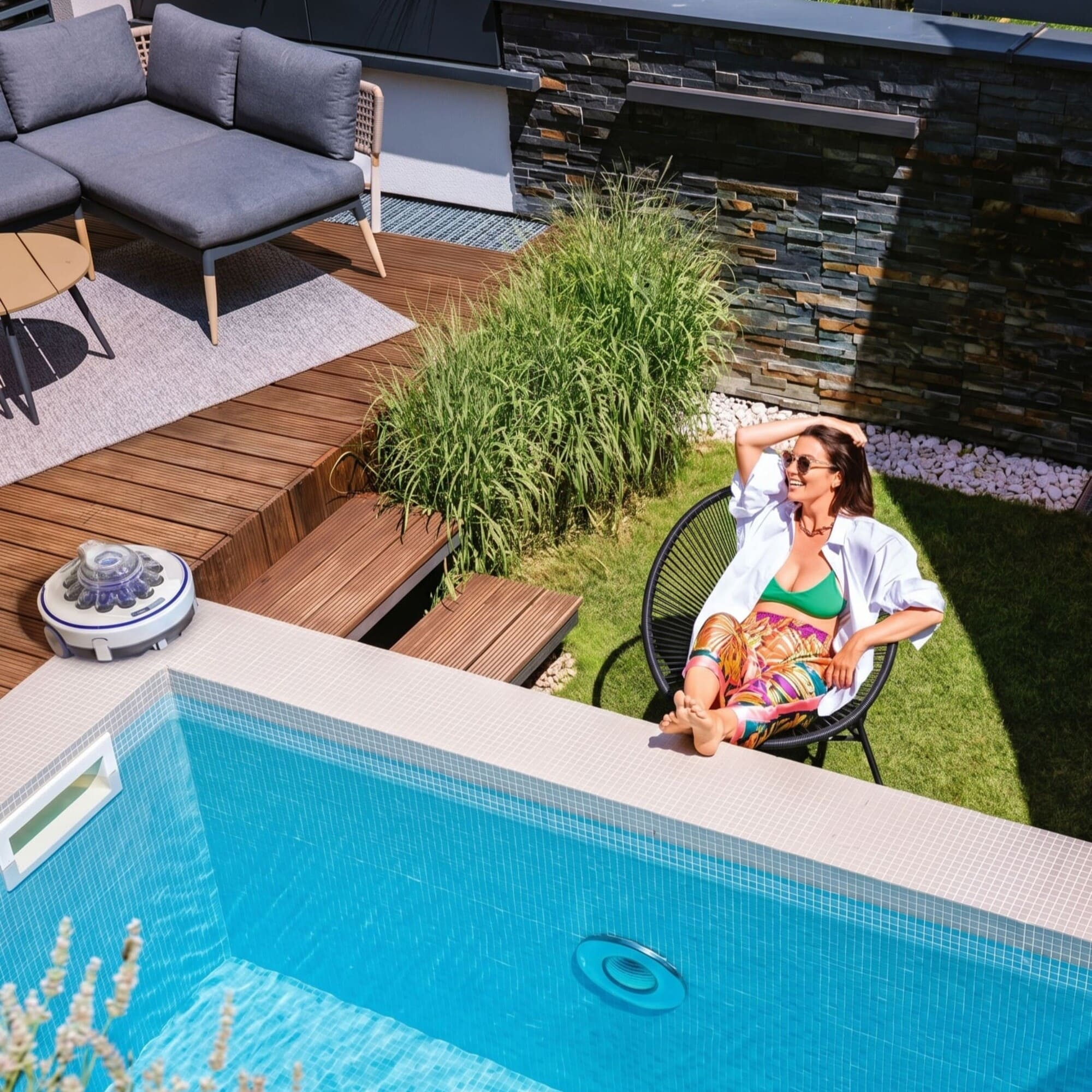 Frau entspannt sich am Pool neben einem Roboterreiniger und Gartenmöbeln.