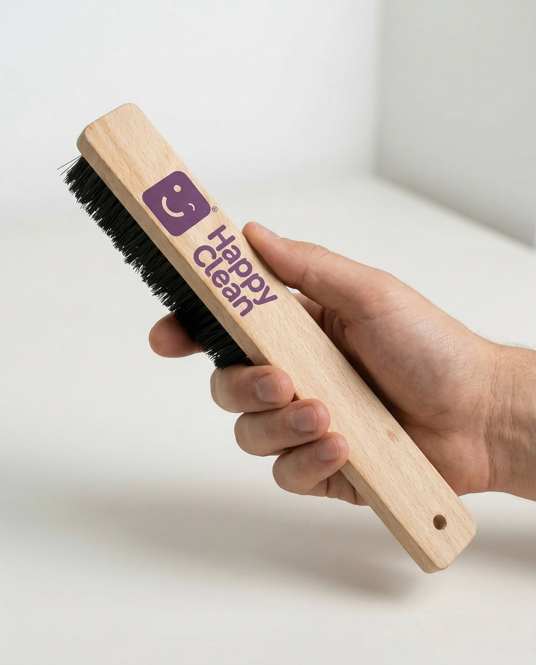 Een hand houdt een houten borstel vast met paars Happy Clean logo en zwarte borstels.