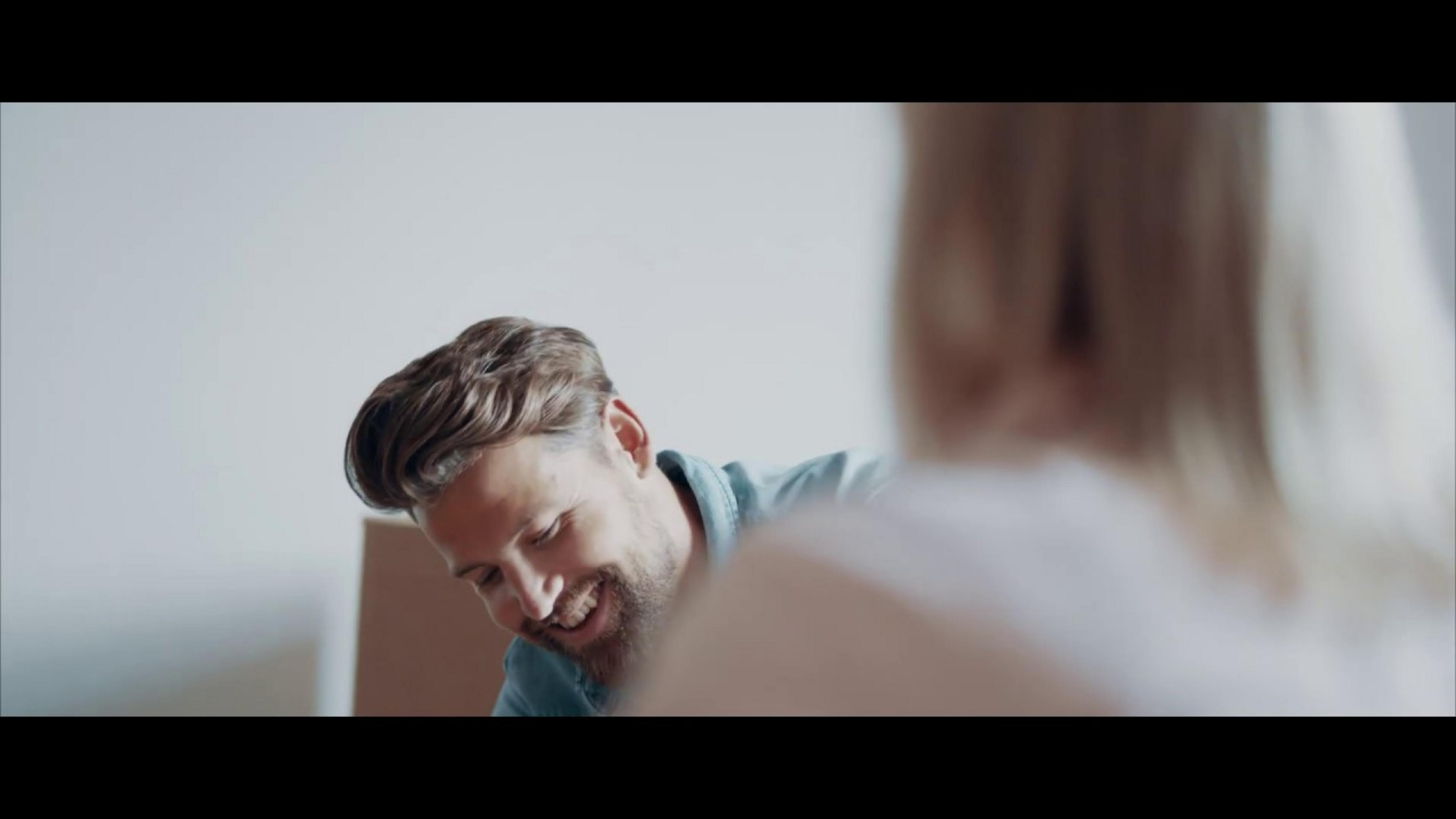 Un uomo con la barba sorride, una persona in primo piano è sfocata.