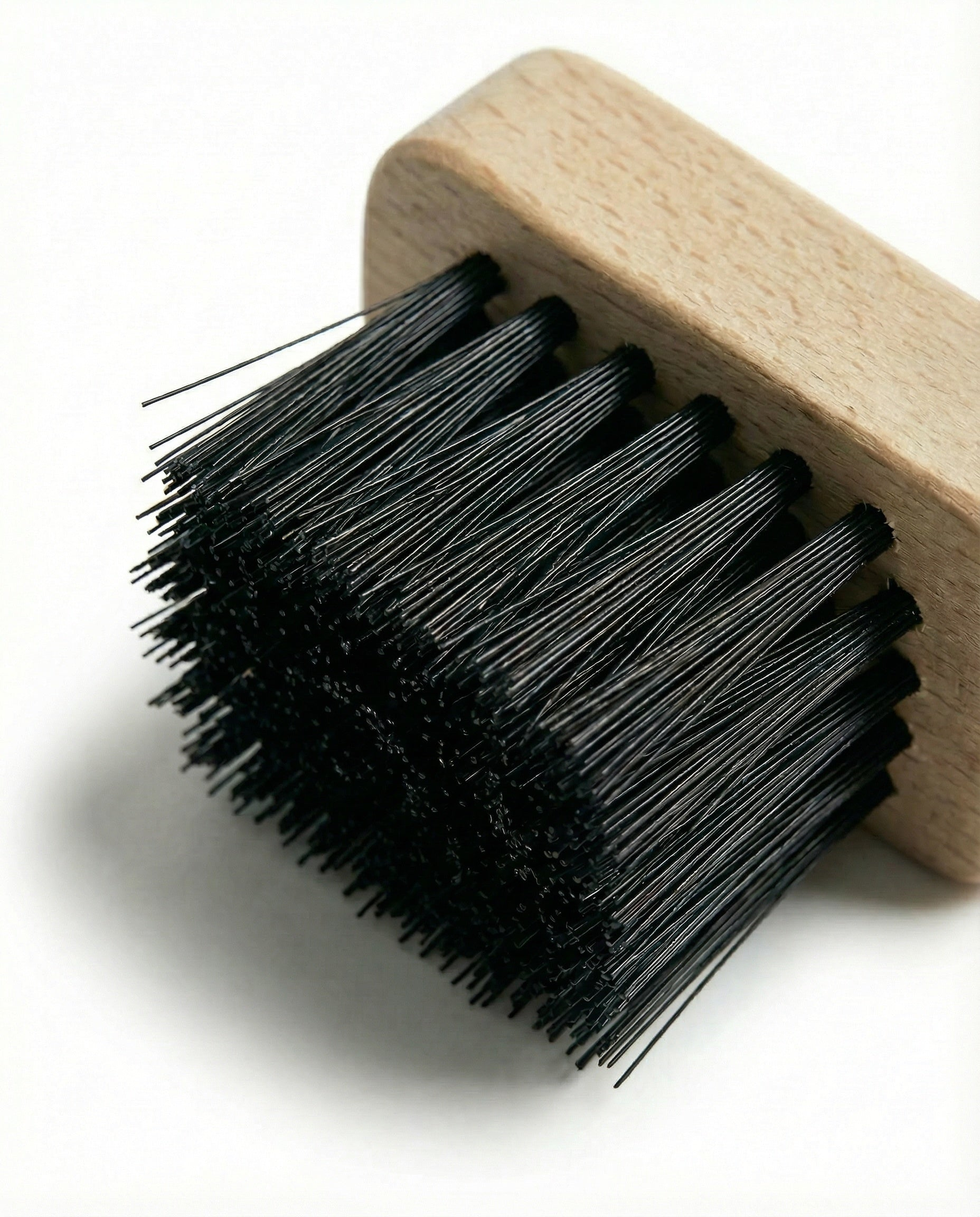Een houten schoenborstelkop met zwarte borstels op een witte achtergrond.
