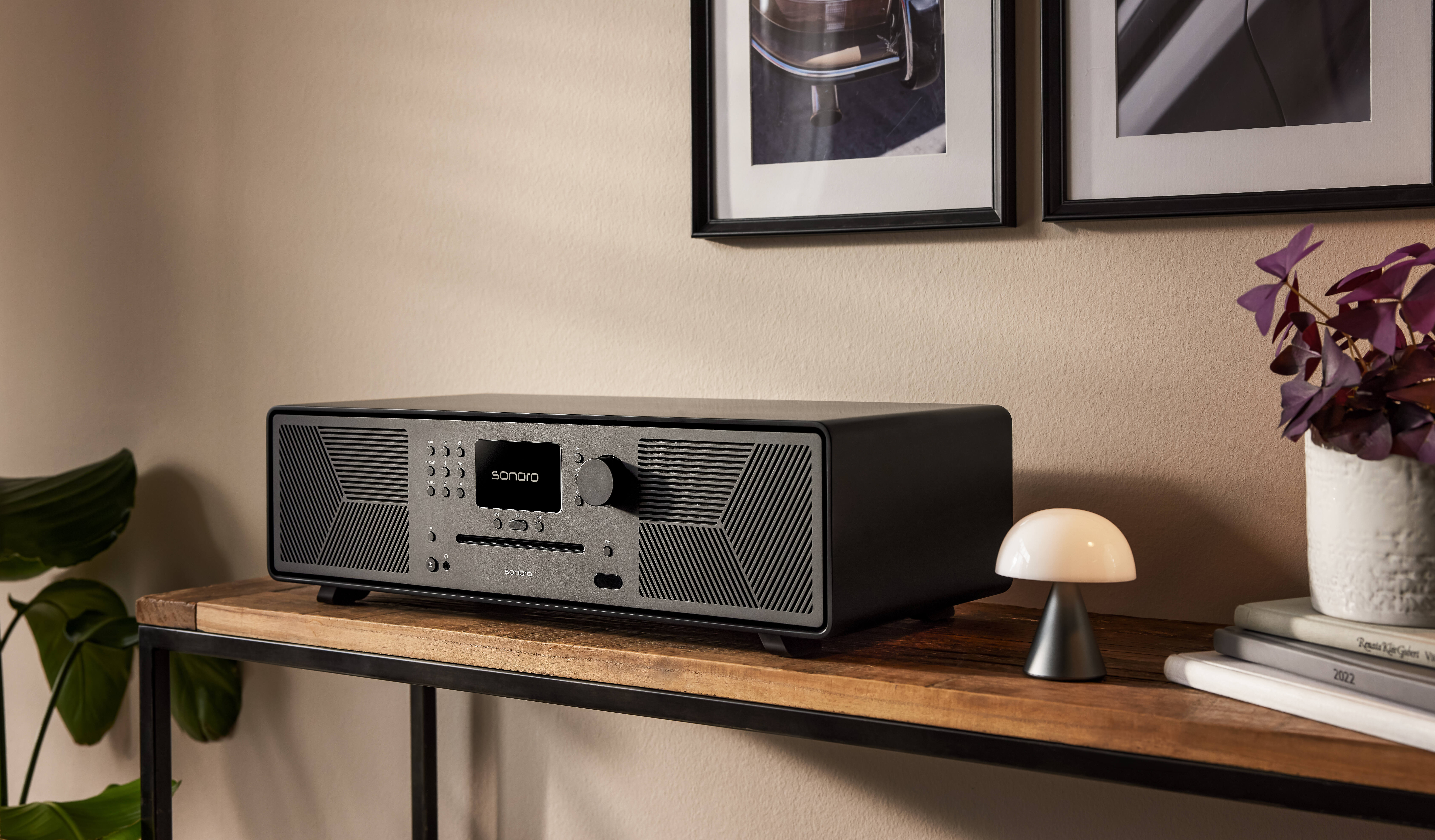 Ein schwarzes Radio steht auf einem Holztisch mit zwei gerahmten Bildern an der Wand.