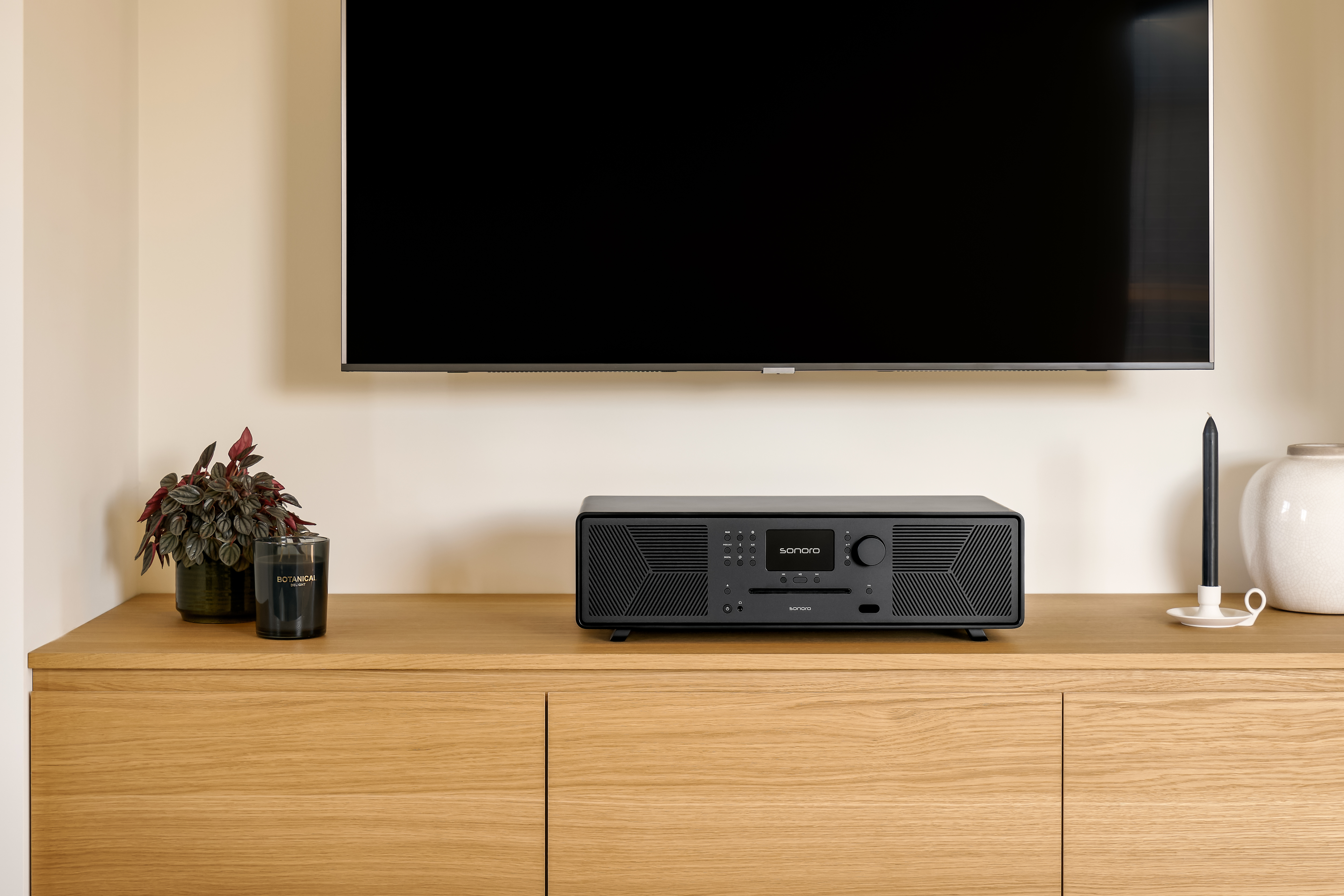 Ein schwarzer Stereo-Receiver steht auf einem Holzschrank unter einem schwarzen Fernseher.