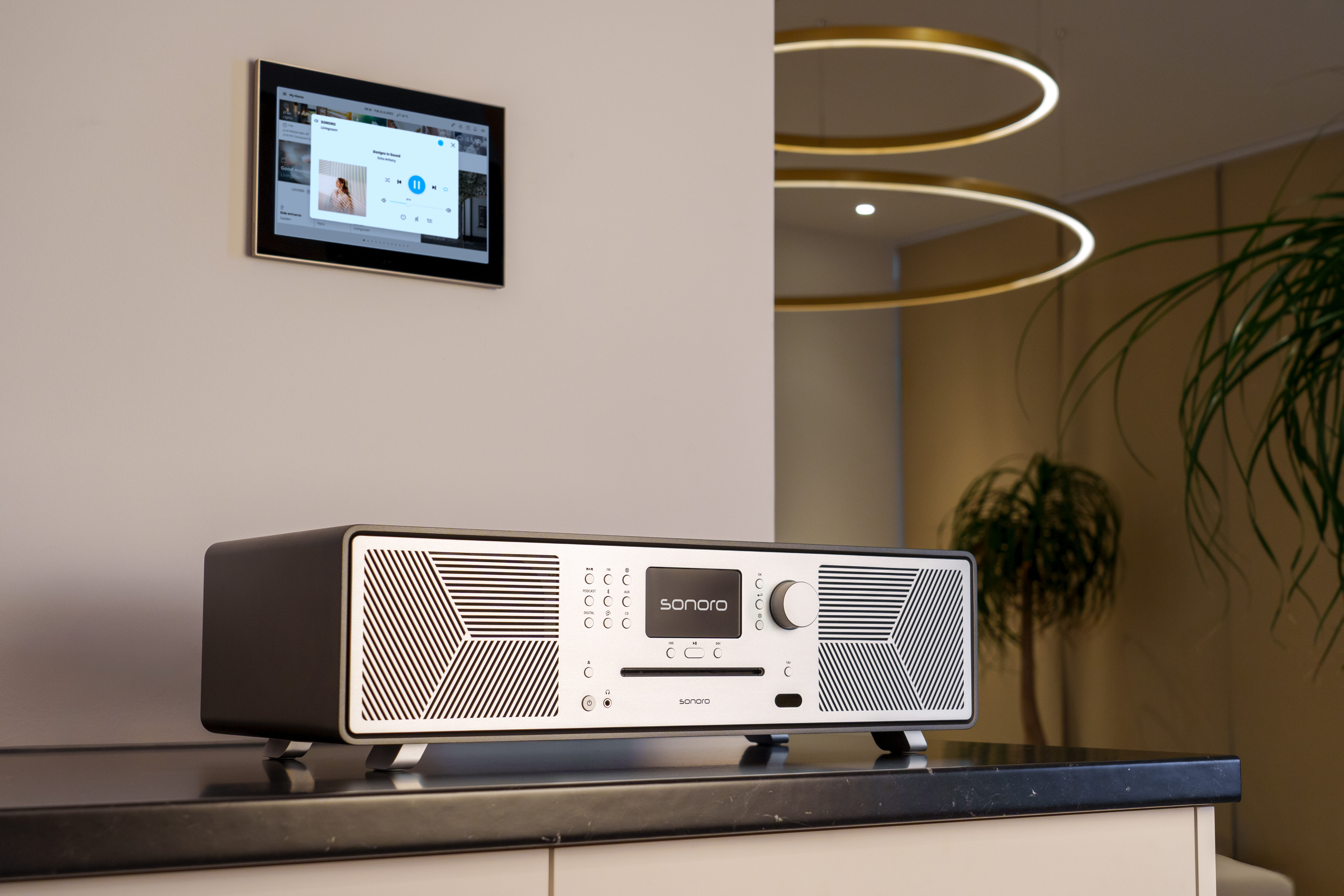 Ein Sonoro-Radio mit CD-Player steht auf einem dunklen Tisch. Eine Wandmontage-Steuerkonsole ist sichtbar.