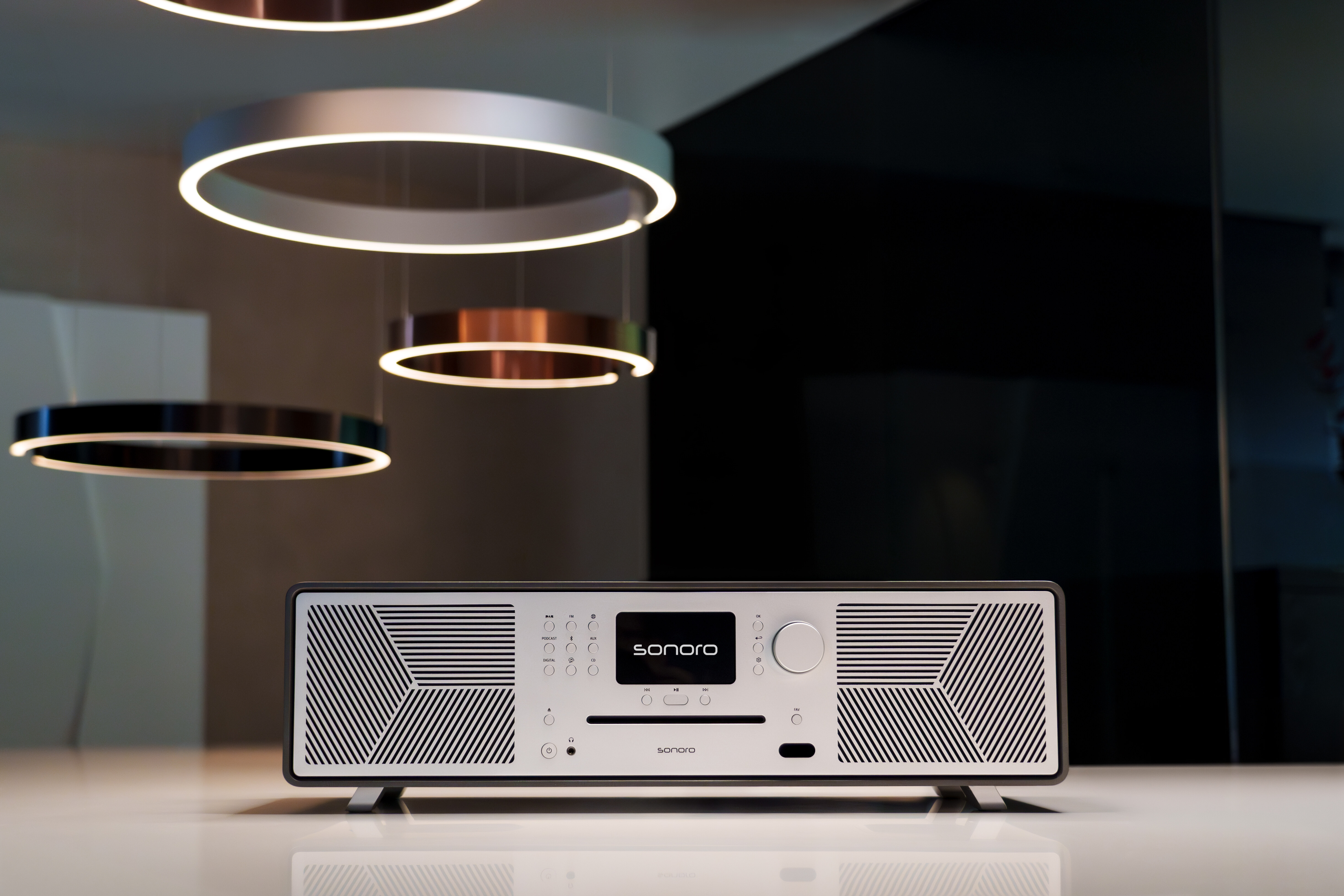 Ein modernes Radio mit CD-Player und Lautsprechern steht auf einem Tisch. Hängende Lampen sind im Hintergrund.