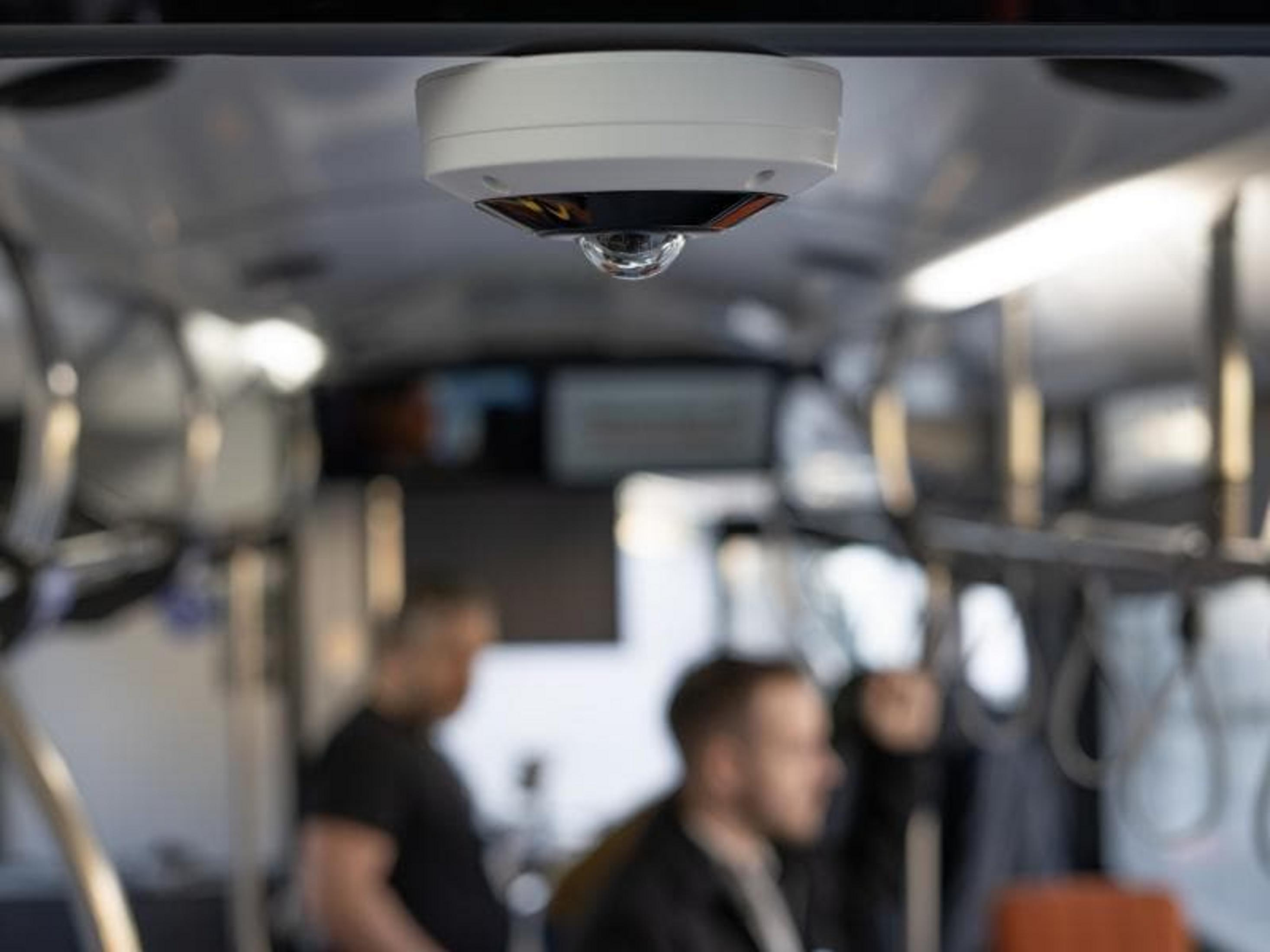 Una telecamera di sicurezza bianca è montata sul soffitto di un autobus sopra i passeggeri.