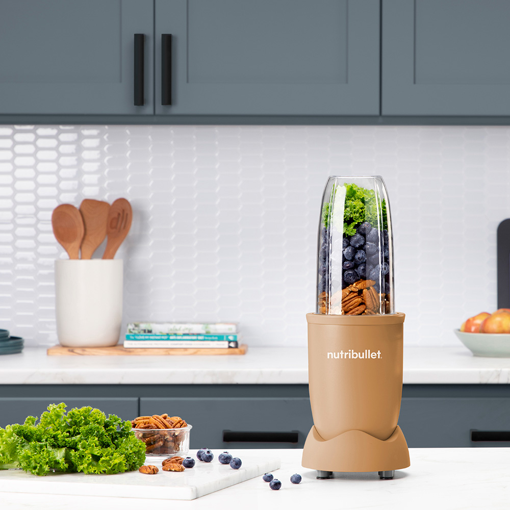 A Nutribullet blender with blueberries, kale, and pecans on a kitchen counter.